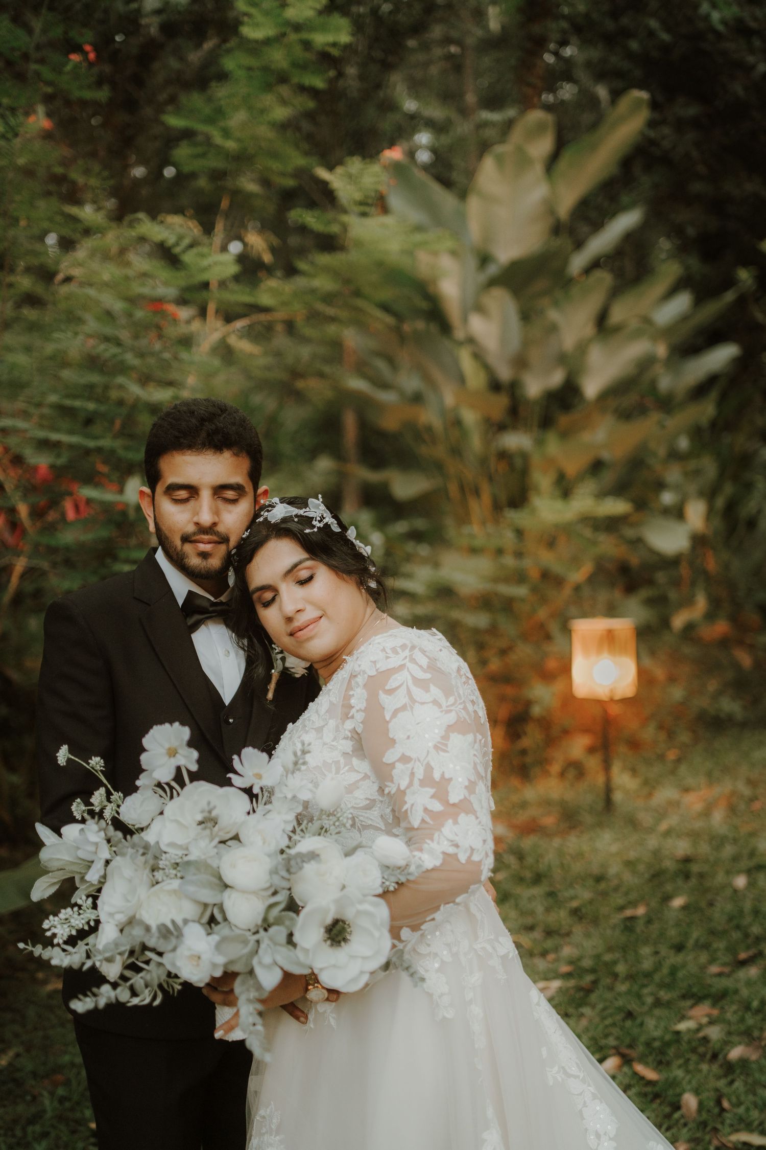 A tender wedding moment captured in a garden with warm evening light and lanterns.