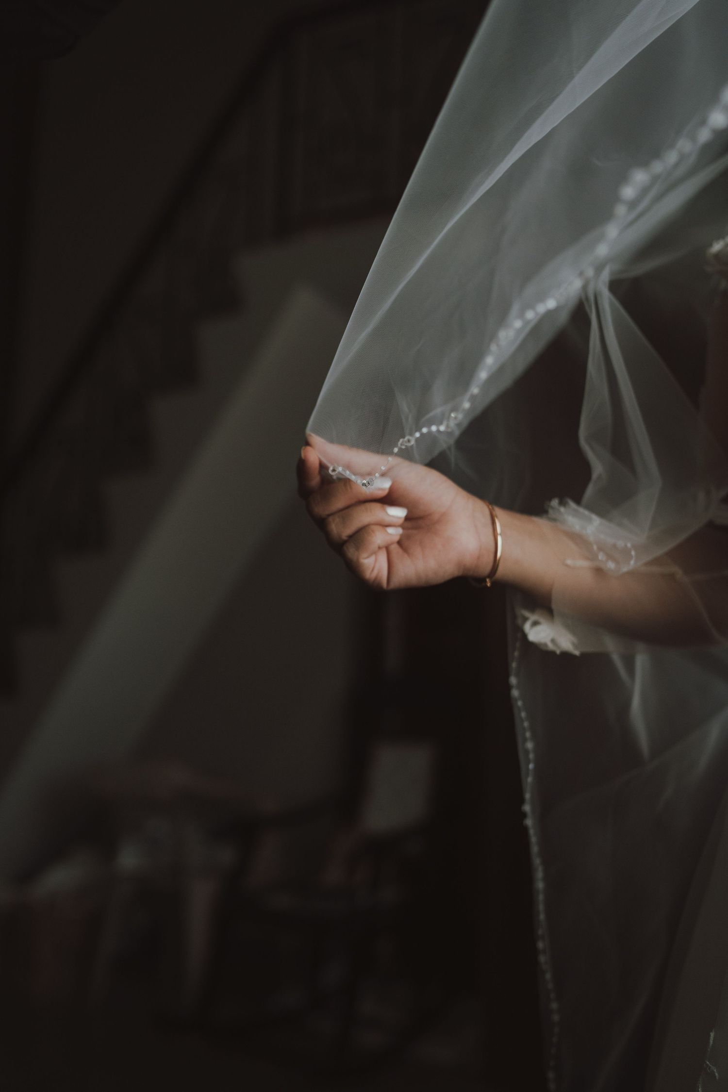 A close-up detail shot of hands holding a delicate wedding veil with beaded trim.