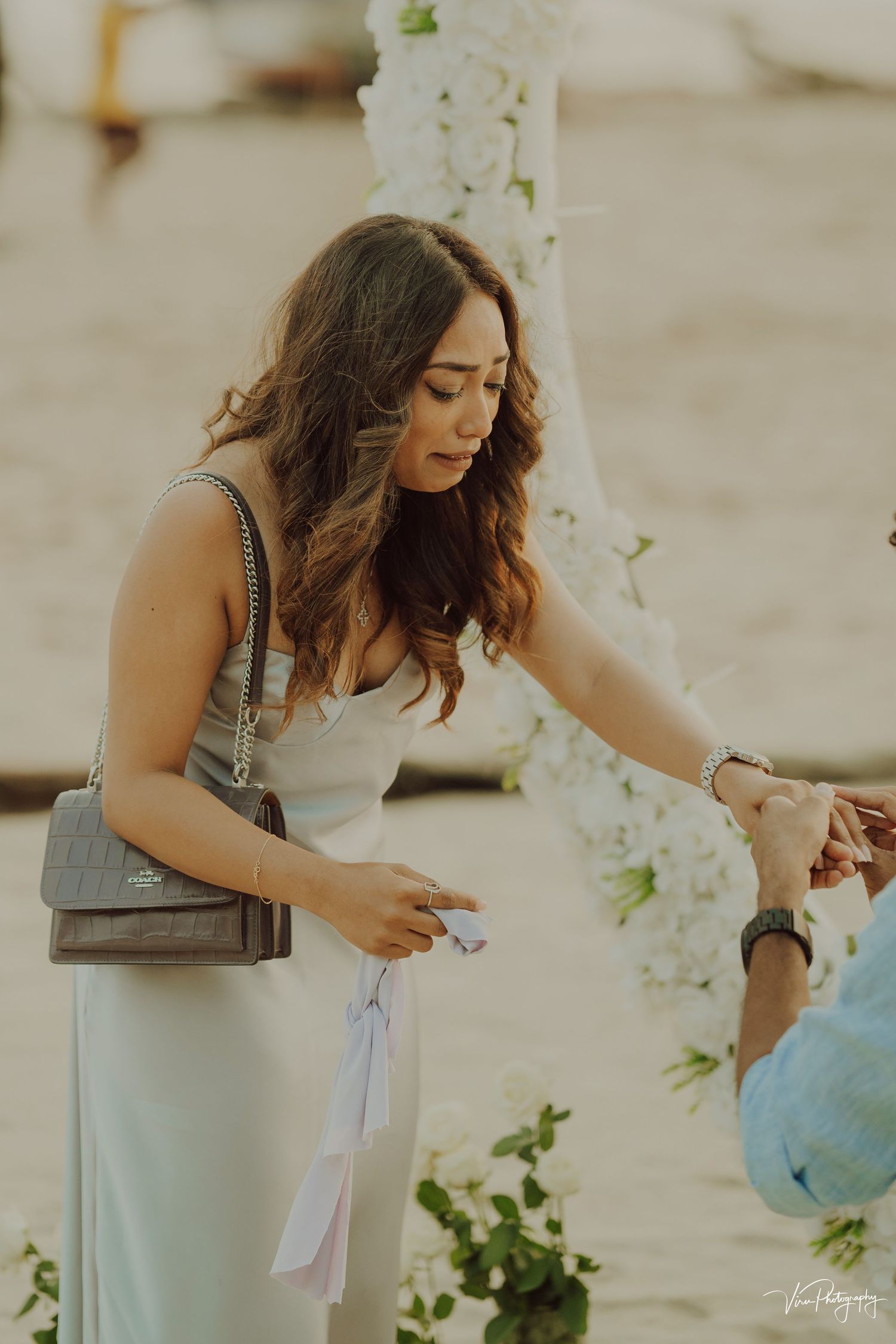 A guest in a flowing white dress reaches down during an elegant outdoor event decorated with white floral arrangements.
