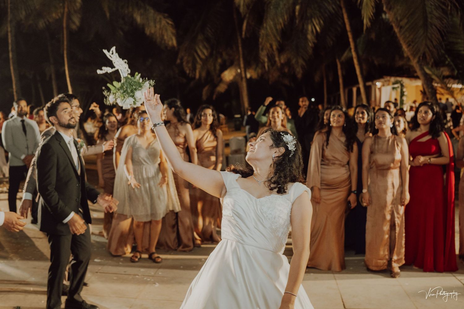 Wedding celebration at night with dancing and celebration on an illuminated outdoor dance floor under palm trees.