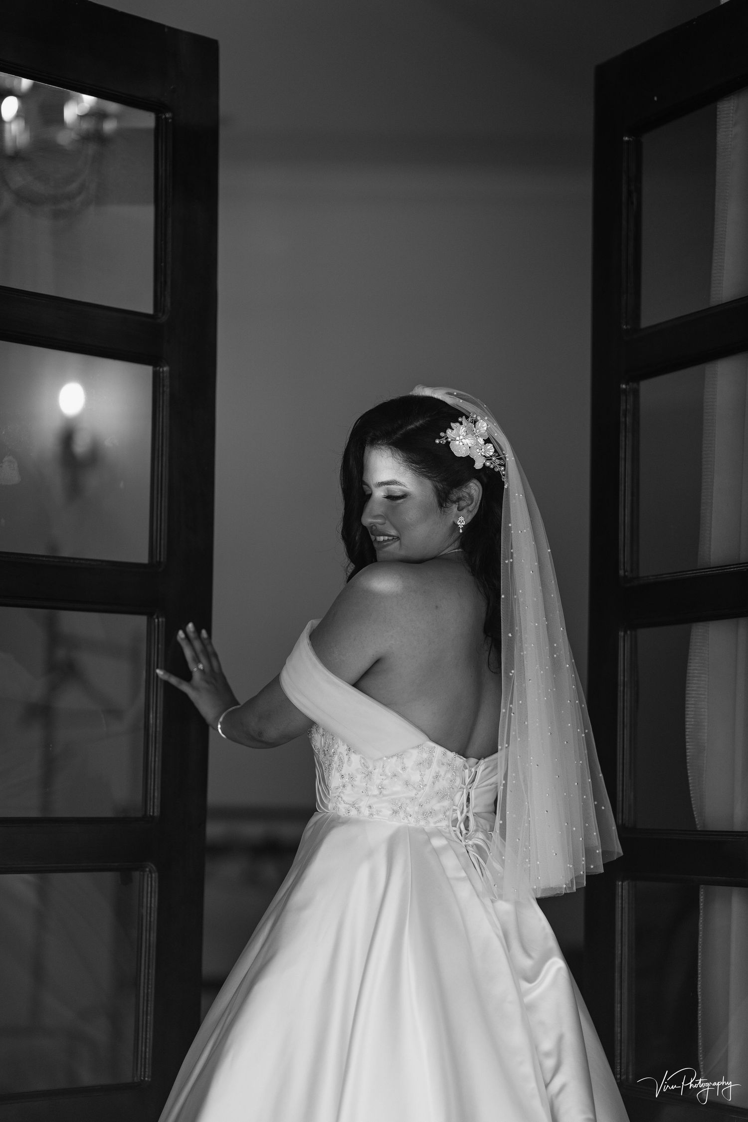 Black and white bridal portrait from behind showing an elegant strapless wedding gown with lace details and flowing veil.