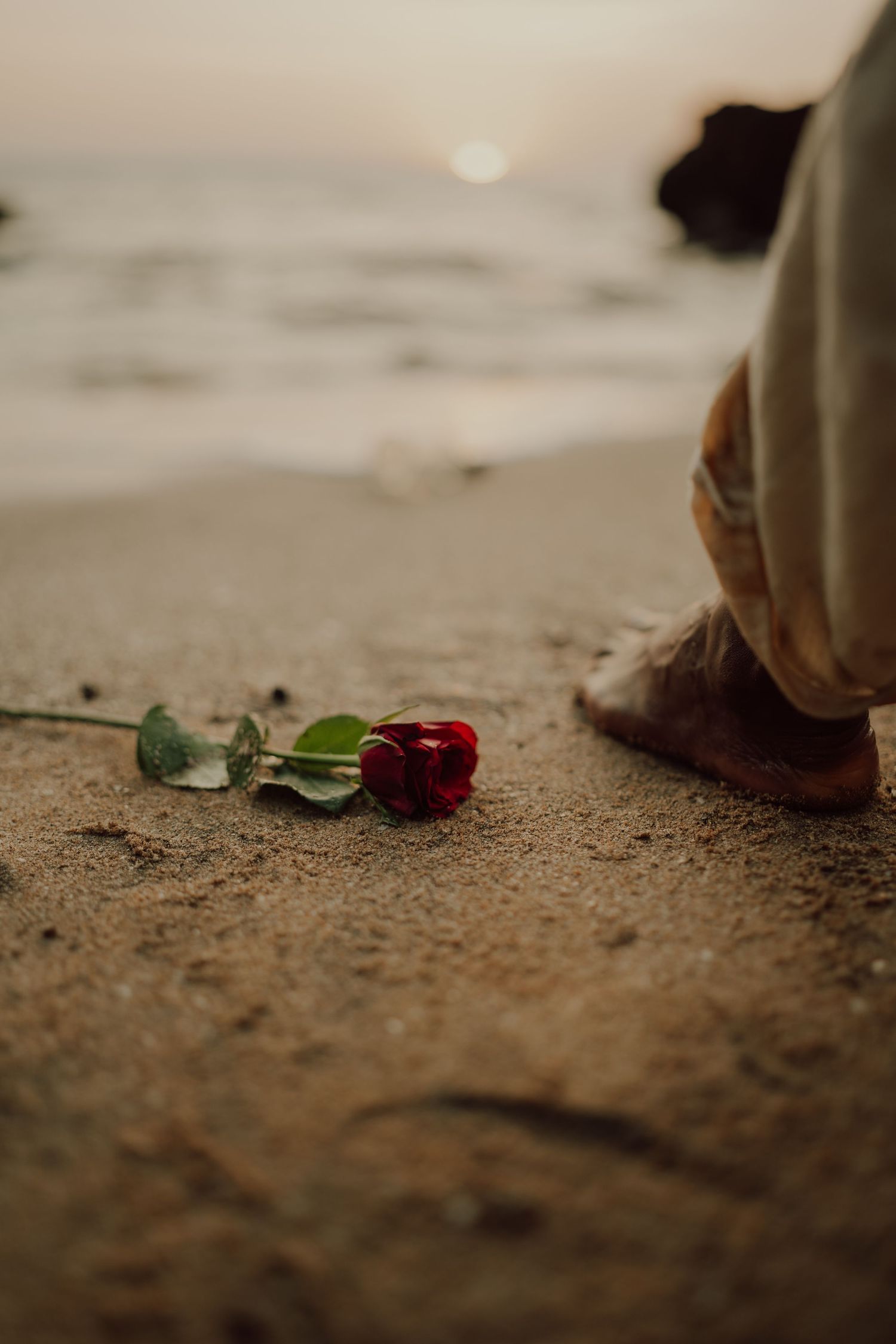 Small pieces of sea glass and shells scattered on sandy beach with feet walking past in soft focus.