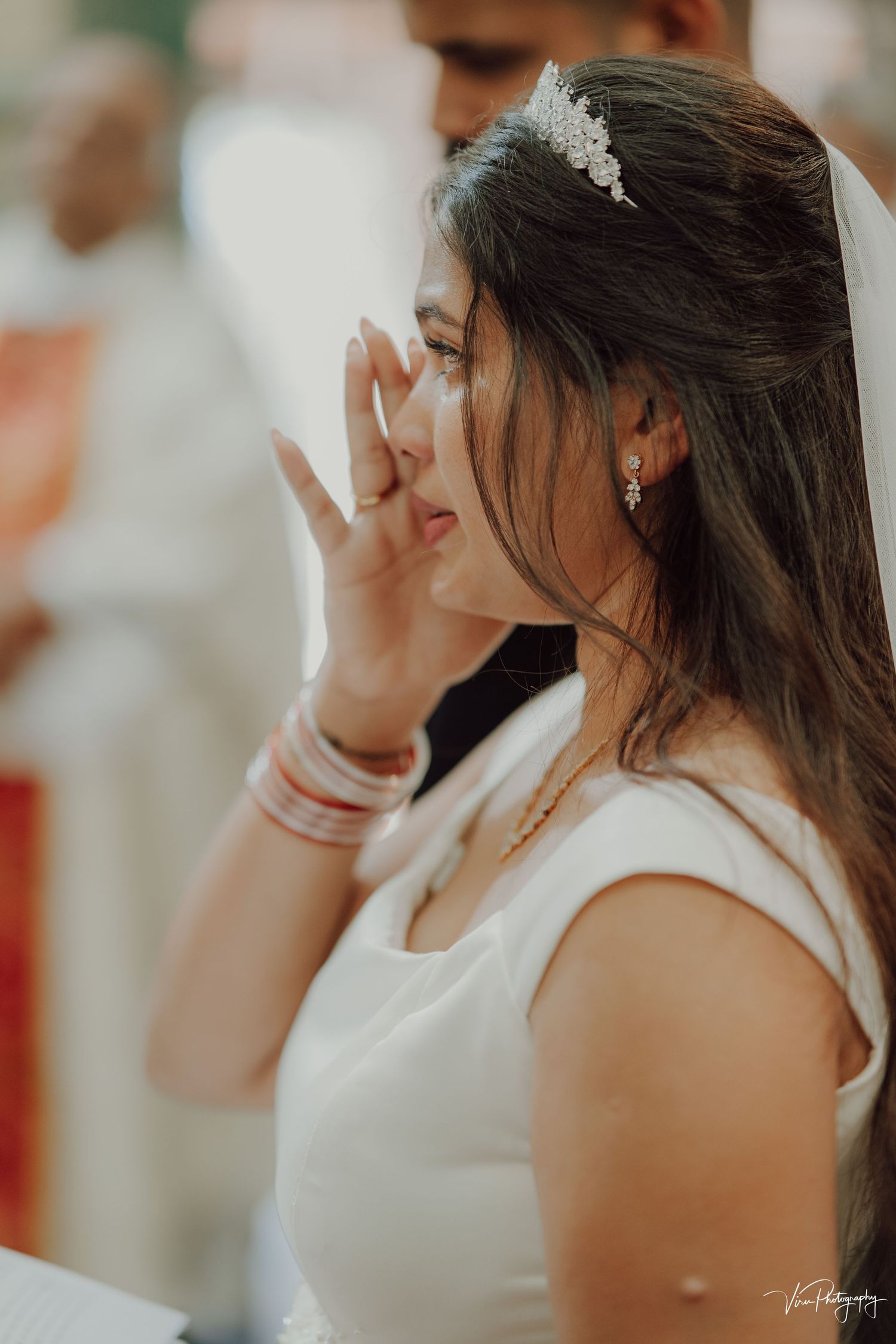 A bride wearing a white dress and delicate hair accessory wipes away tears during an emotional wedding moment.
