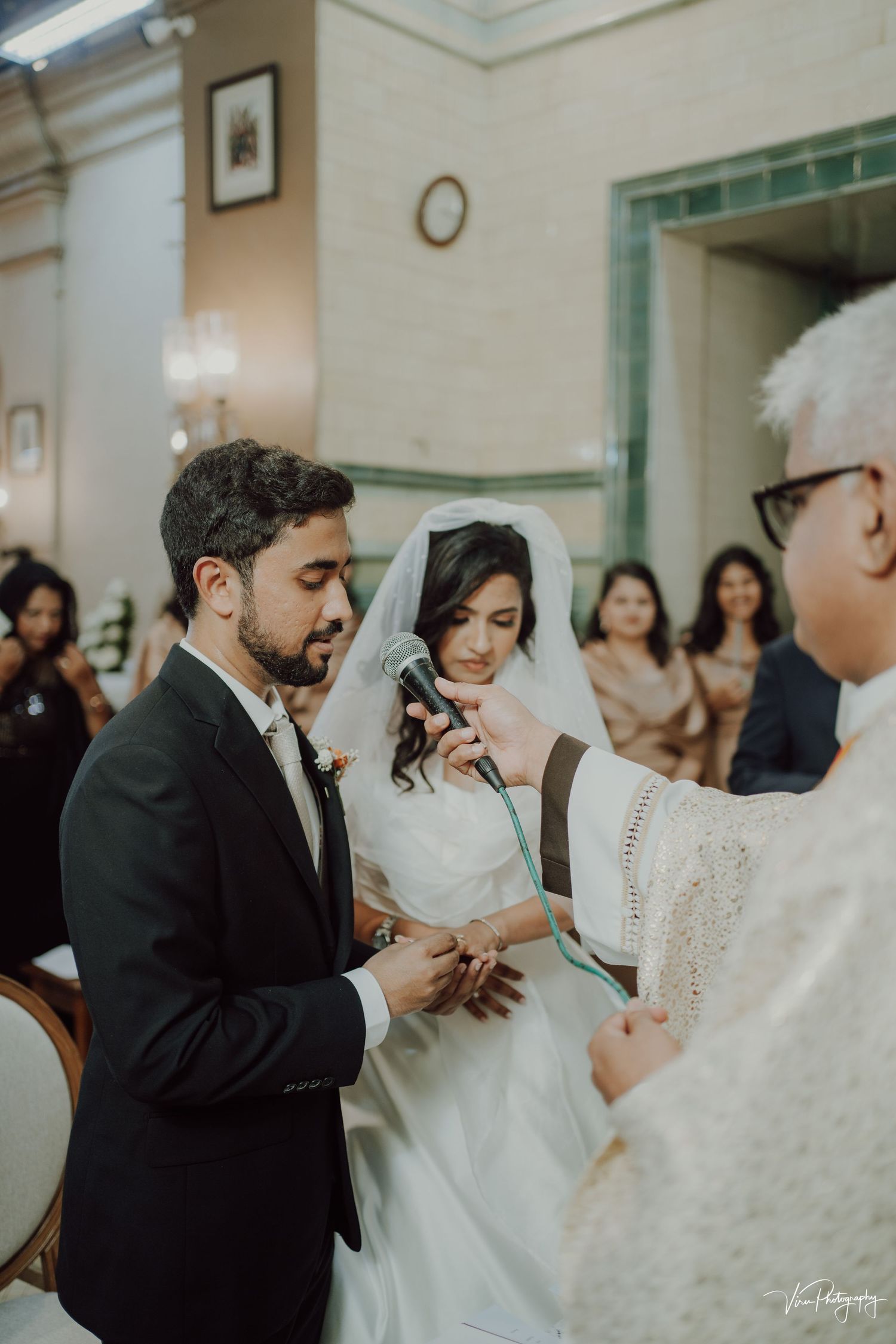 A couple participates in a traditional indoor wedding ceremony with guests and clergy in a formal church setting.