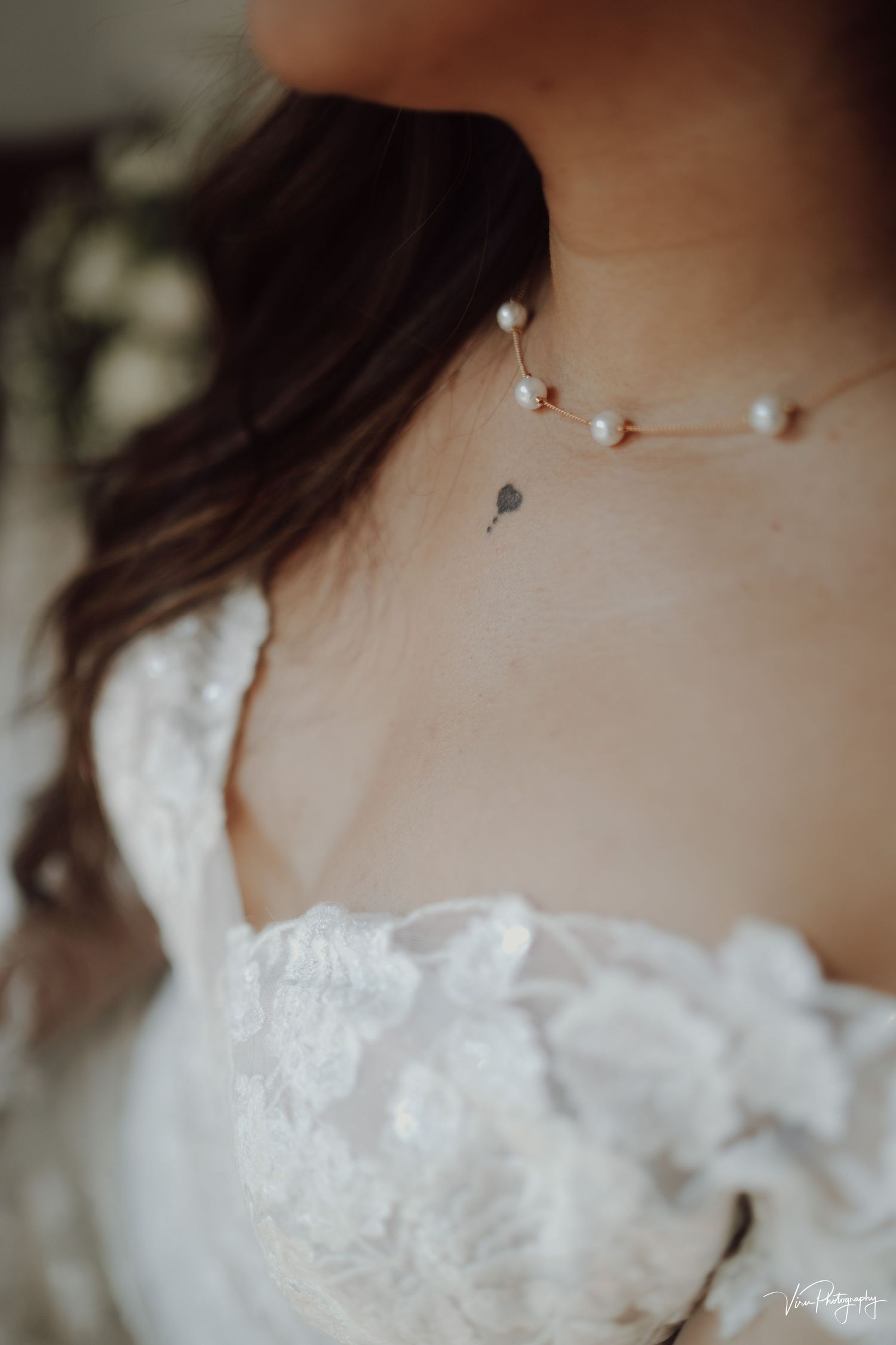 Close-up of delicate pearl necklace around neck with white lace dress and dark flowing hair.