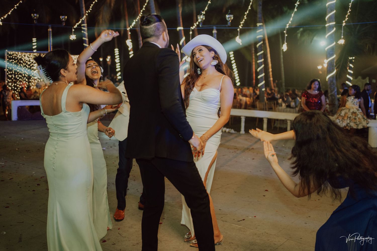 Wedding guests dancing energetically on the dance floor during a reception with festive lighting and decor.