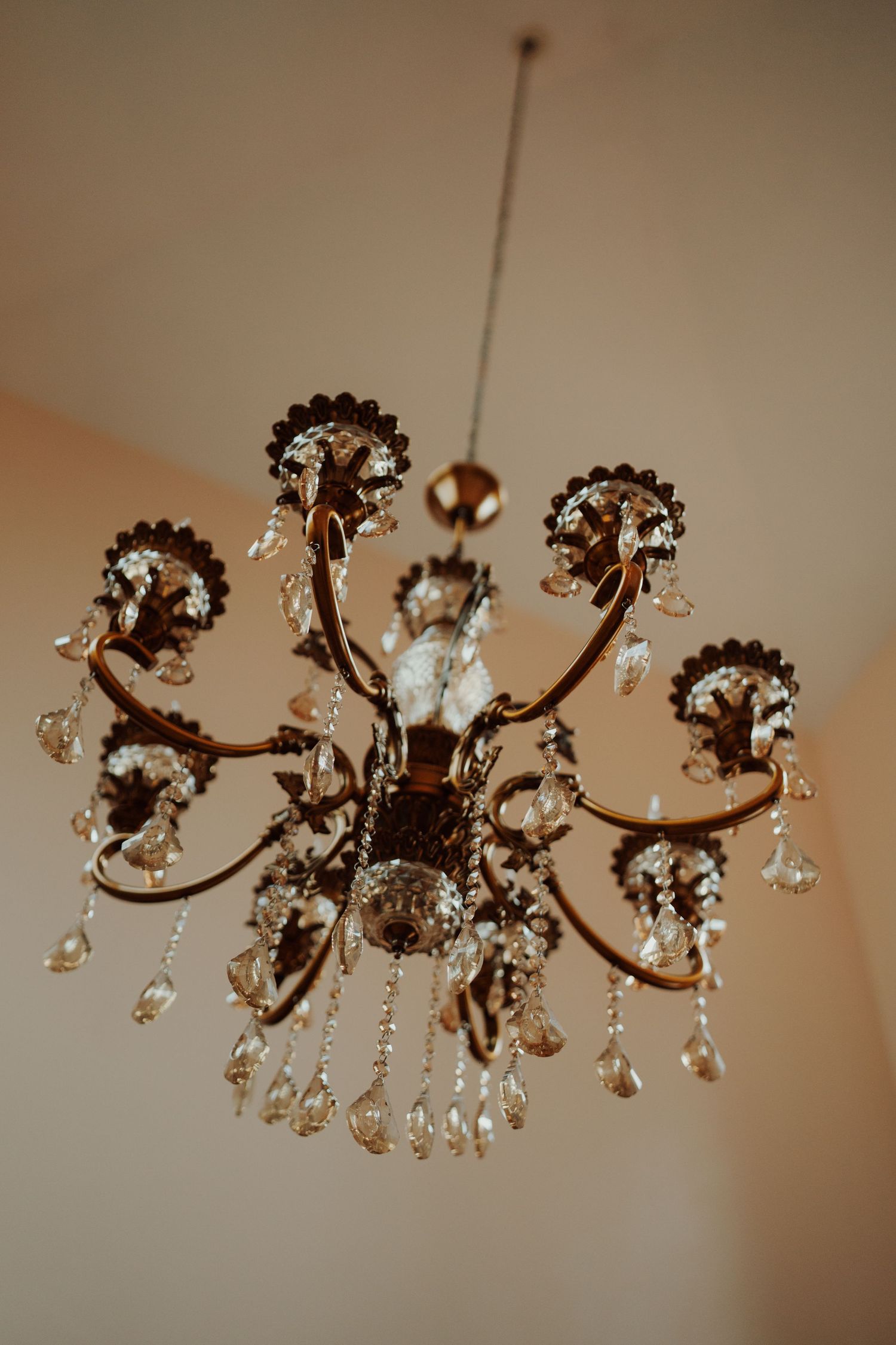 Ornate bronze chandelier with curved arms and hanging crystal drops suspended from a cream ceiling.
