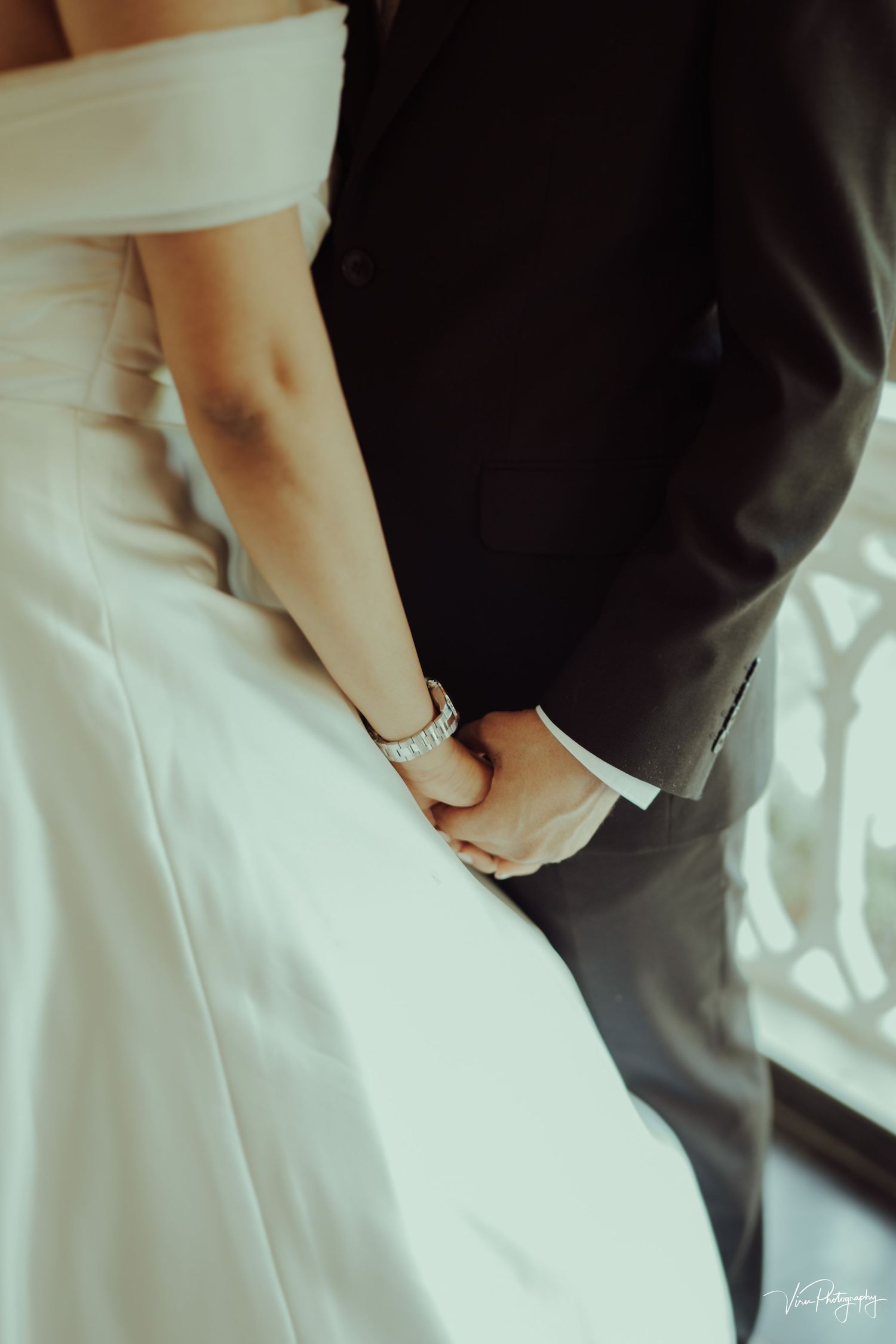Intimate close-up photo of a couple embracing, showing white wedding dress and black suit details.