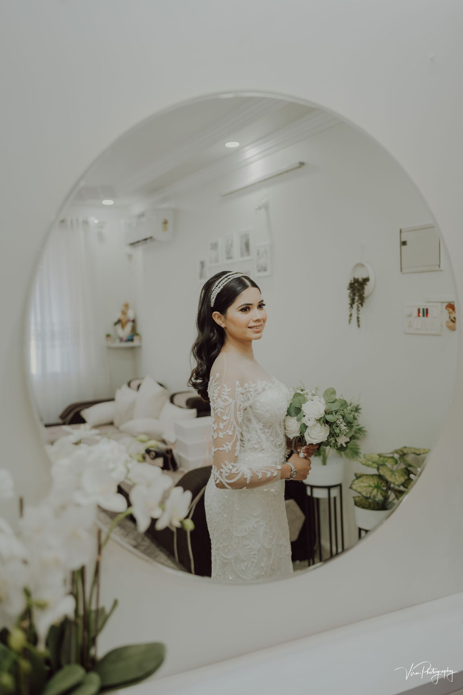 A mirror reflection shows a bride in an elegant lace long-sleeved wedding dress holding a white floral bouquet.
