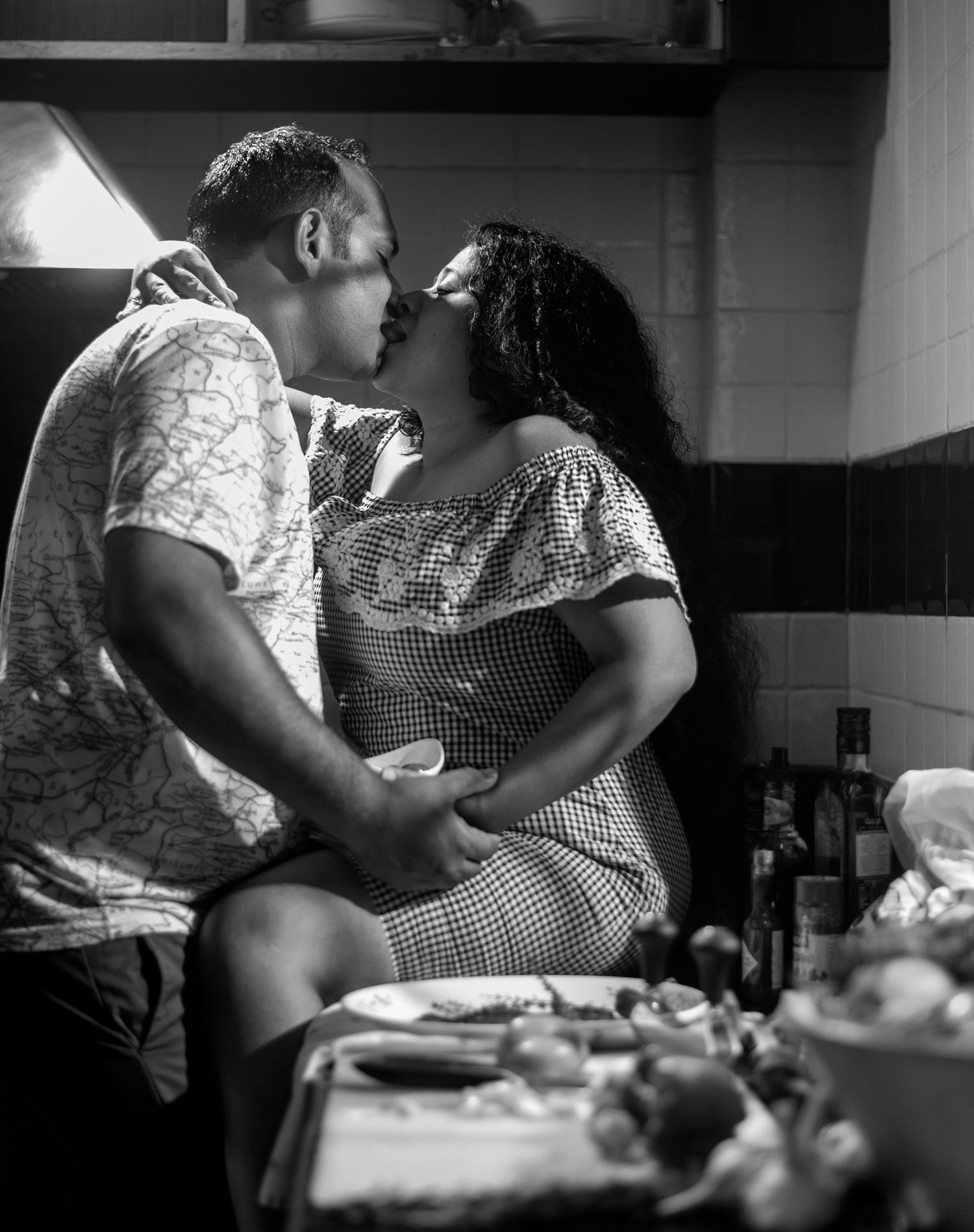 A romantic black and white photograph of a couple sharing an intimate moment in a kitchen setting.
