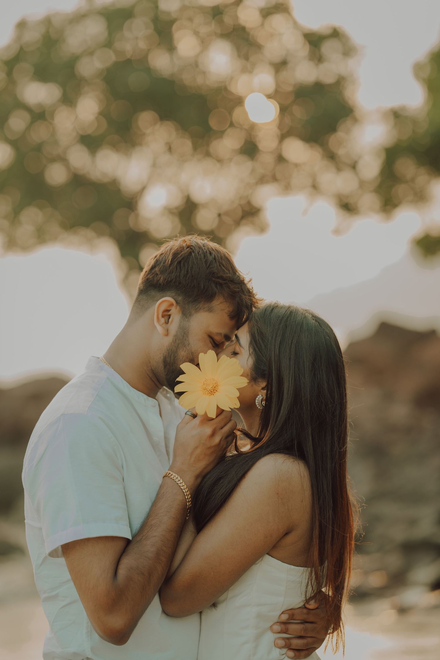 A romantic couple shares tender kisses in a dreamy outdoor setting with soft bokeh lighting during golden hour.
