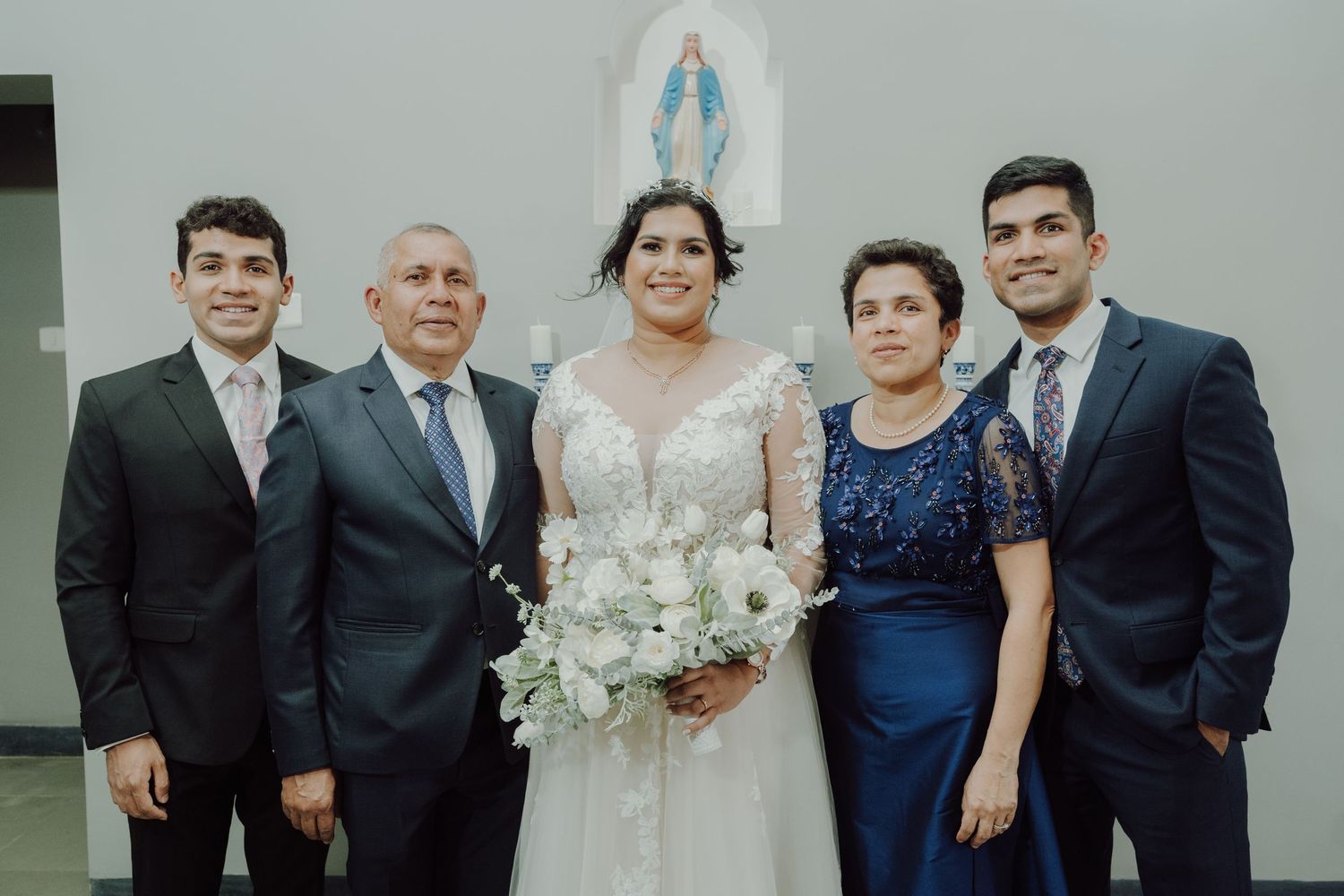 Family group photo with bride and relatives in front of a religious statue.