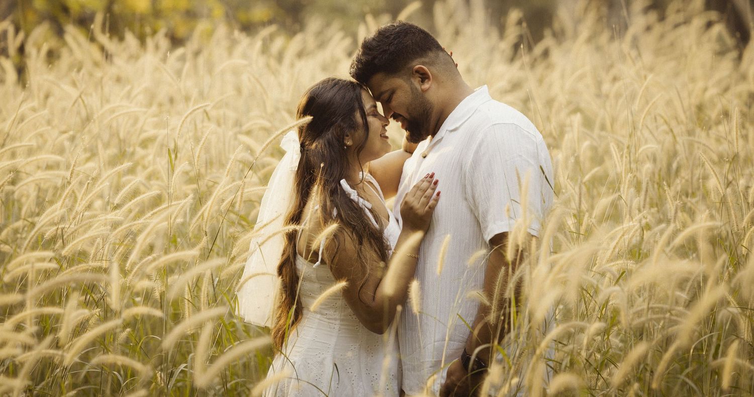Romantic couple embraces tenderly in a golden wheat field during sunset.