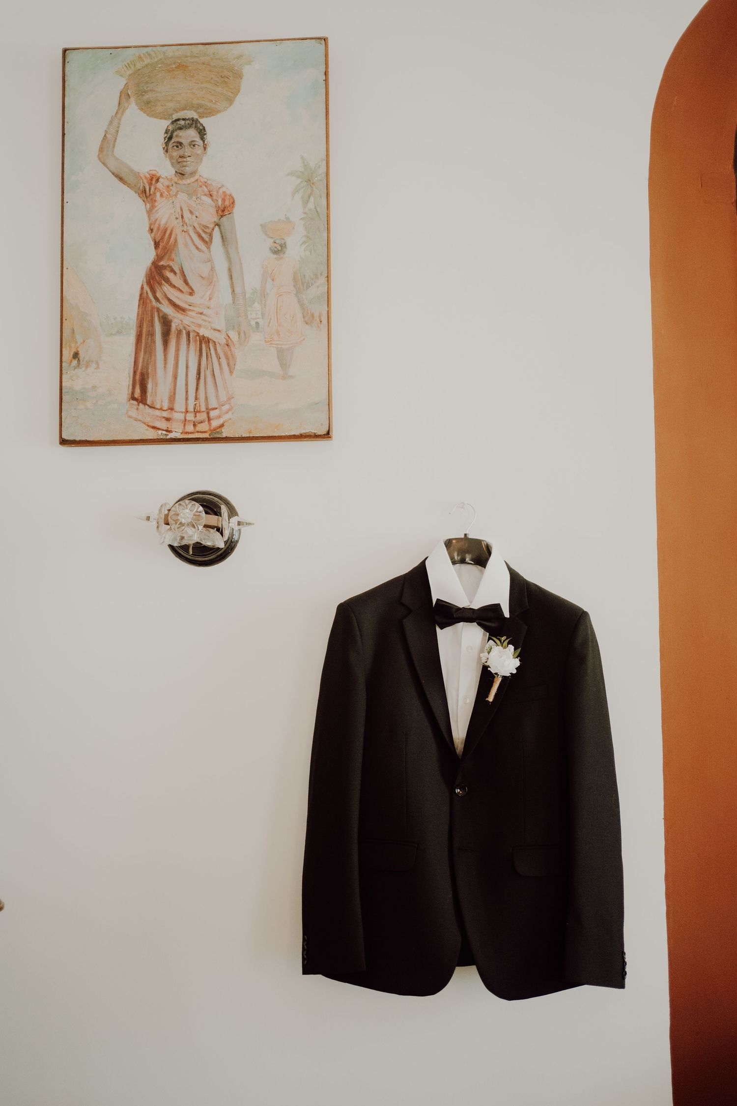 Black suit jacket with white boutonniere hanging against wall with vintage artwork.