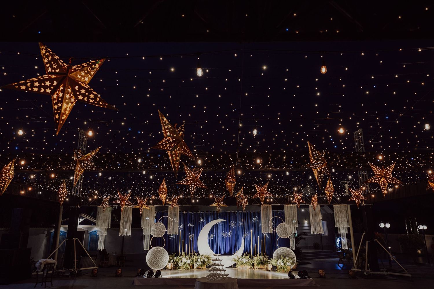 Star-lit outdoor wedding reception setup with crescent moon backdrop and ambient lighting.