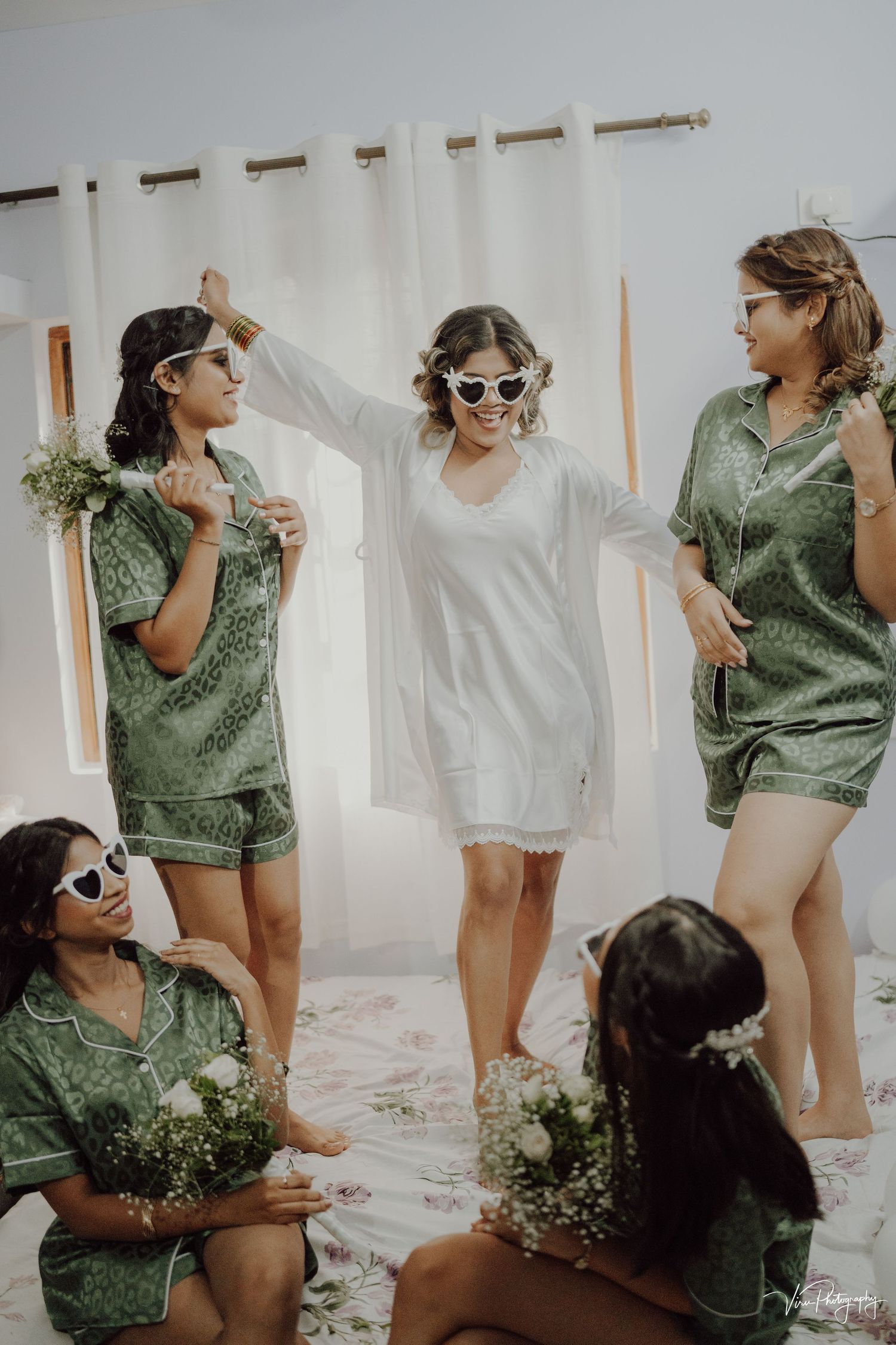 A group wearing matching sage green and white outfits pose together with sunglasses and small floral bouquets.