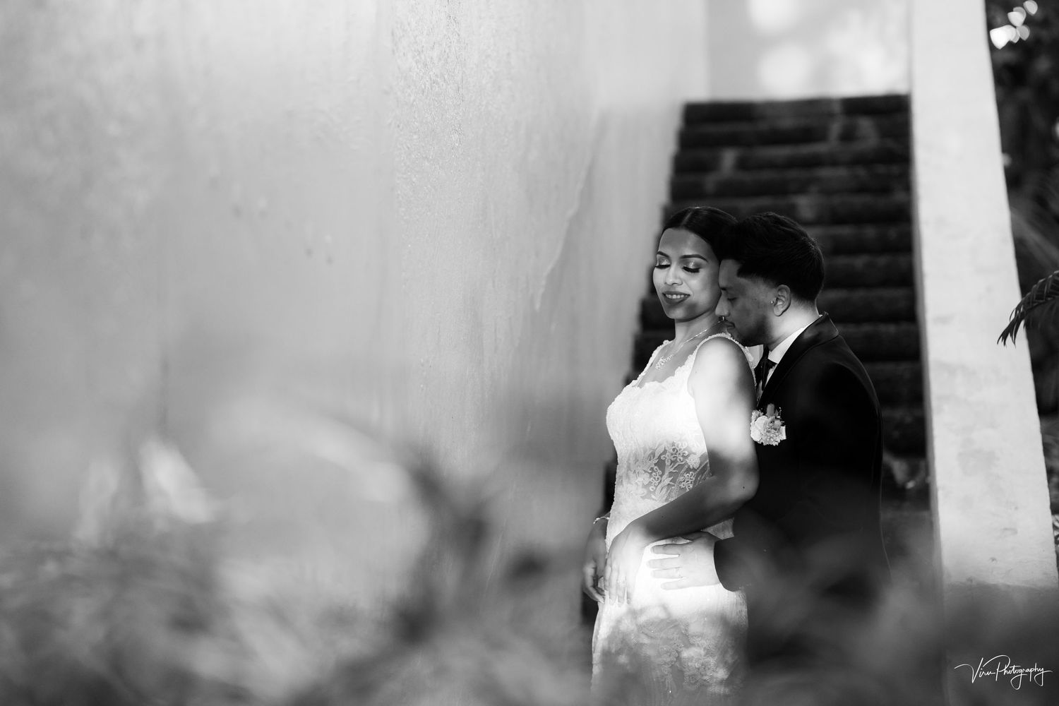 Black and white romantic wedding portrait of a couple at a venue with a dramatic architectural backdrop.