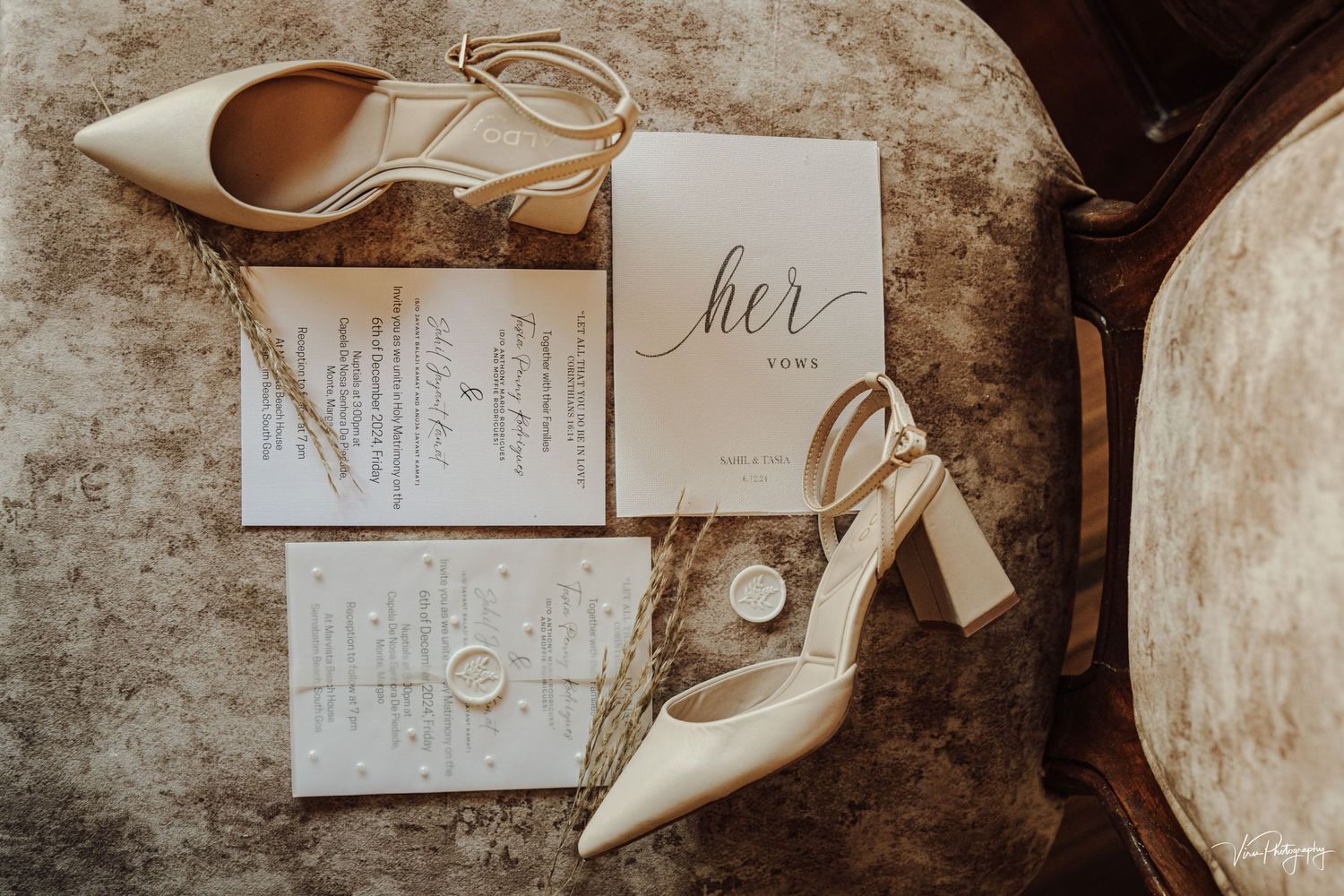 Wedding invitation cards and elegant white heeled shoes arranged on a rustic wooden surface.