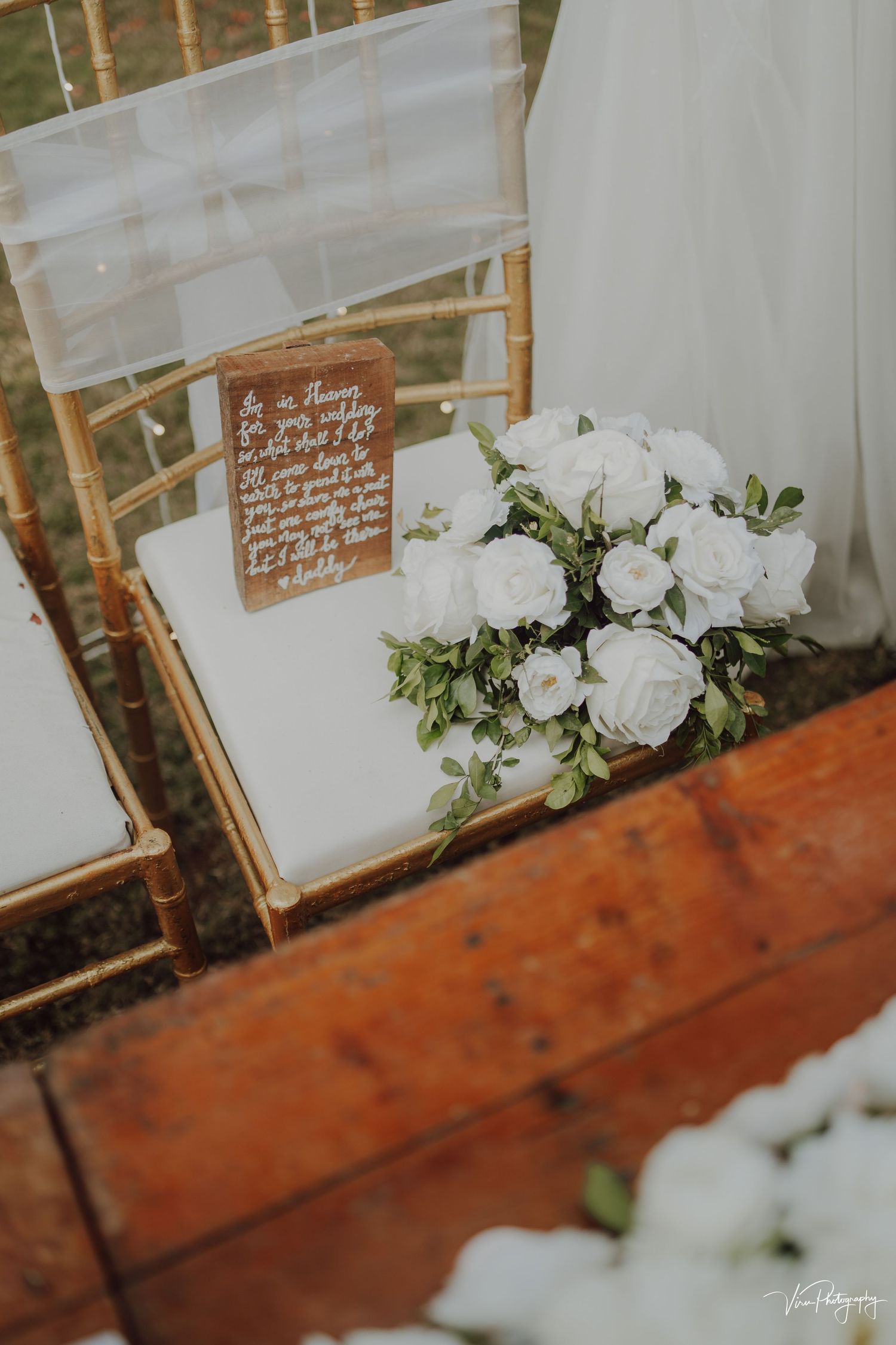 White floral arrangement with wooden signage on a rustic table at an elegant wedding reception setup.