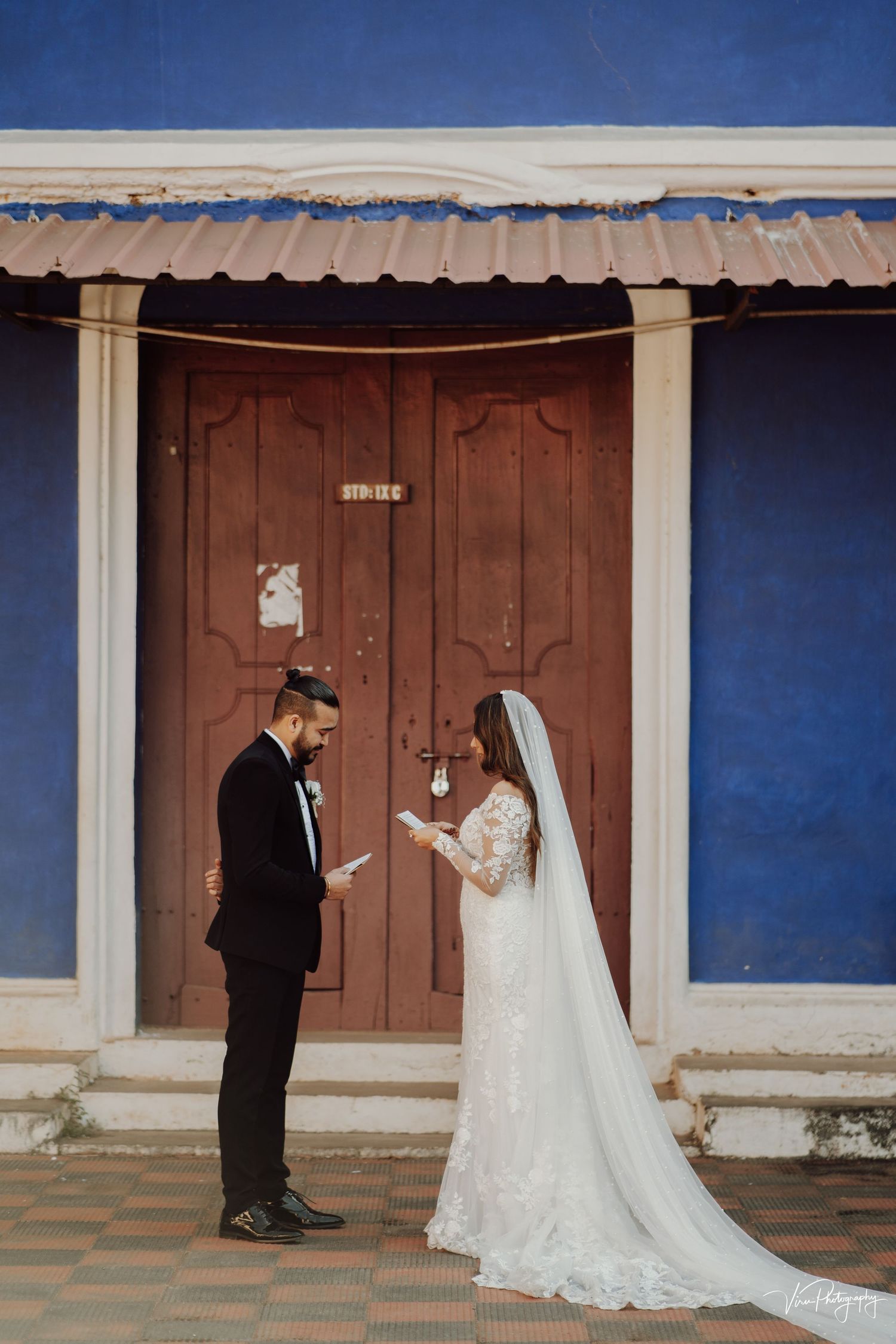 A couple stands together against a rustic blue wall with a brown wooden door on their wedding day.