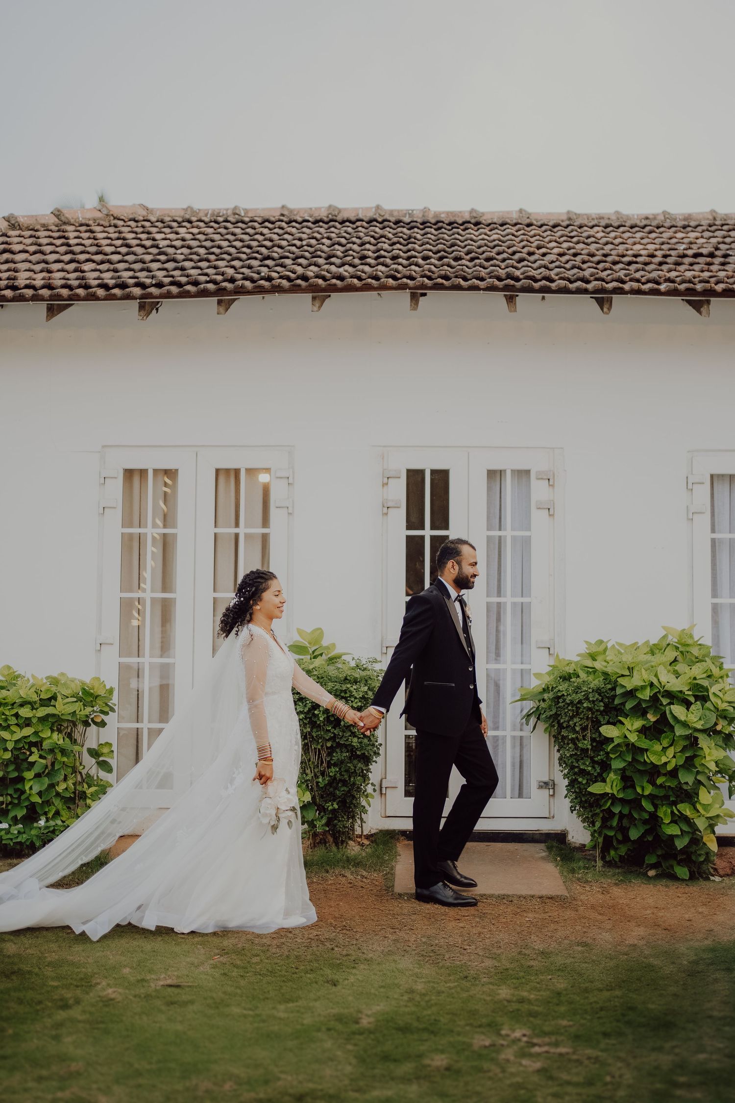 Bride and groom pose playfully with white dress flowing behind an elegant white building with French windows.