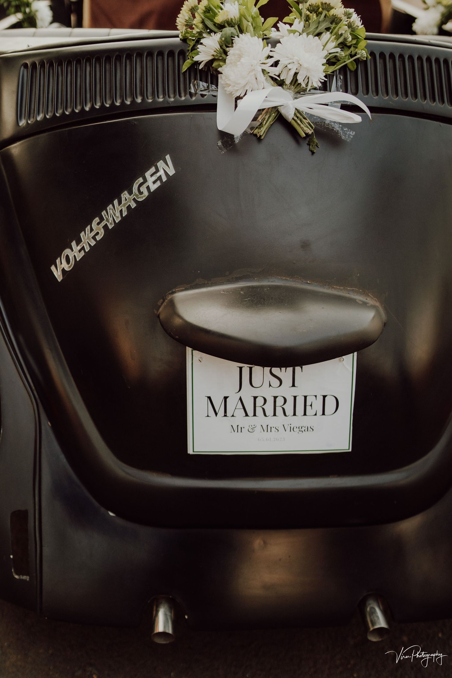 Classic black Volkswagen Beetle decorated with a 'Just Married' sign and floral bouquet at a wedding.
