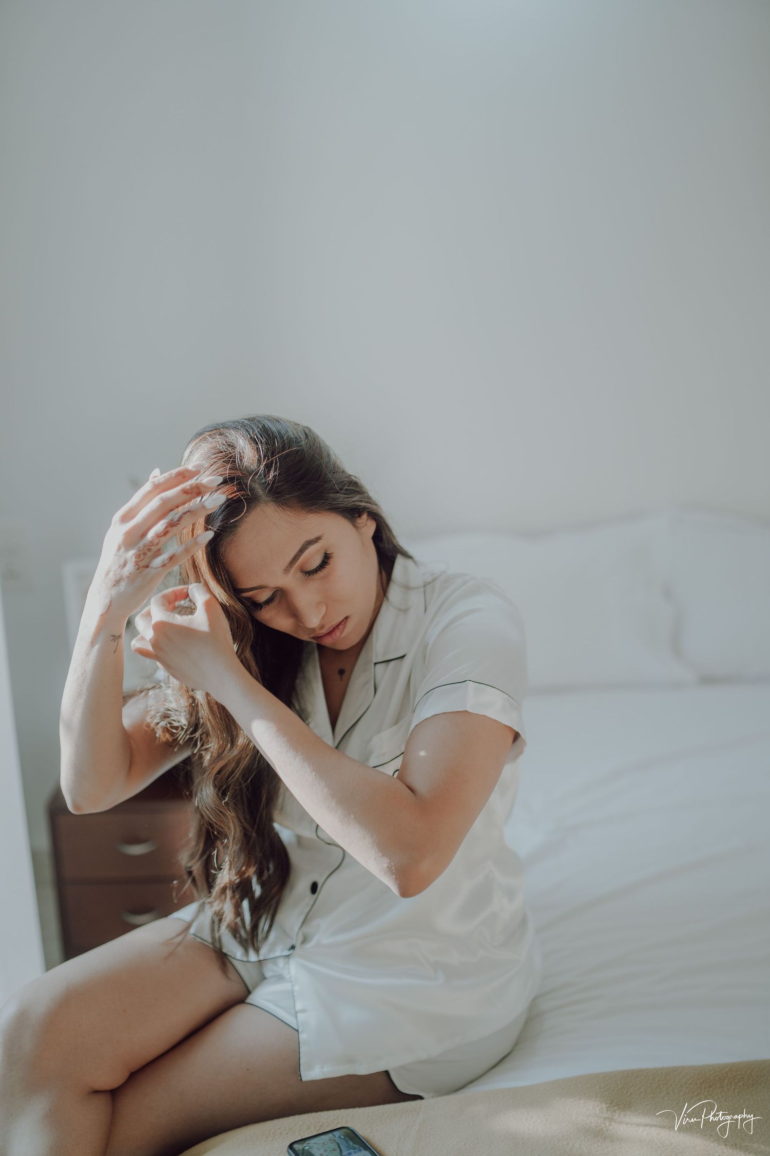 Person in white pajama set sitting on bed with soft lighting in minimalist bedroom setting.