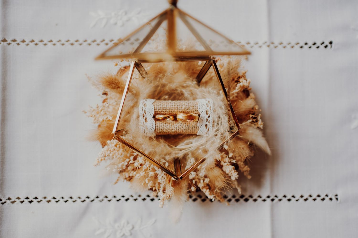 Geometric display holder with wedding rings on delicate lace tablecloth.
