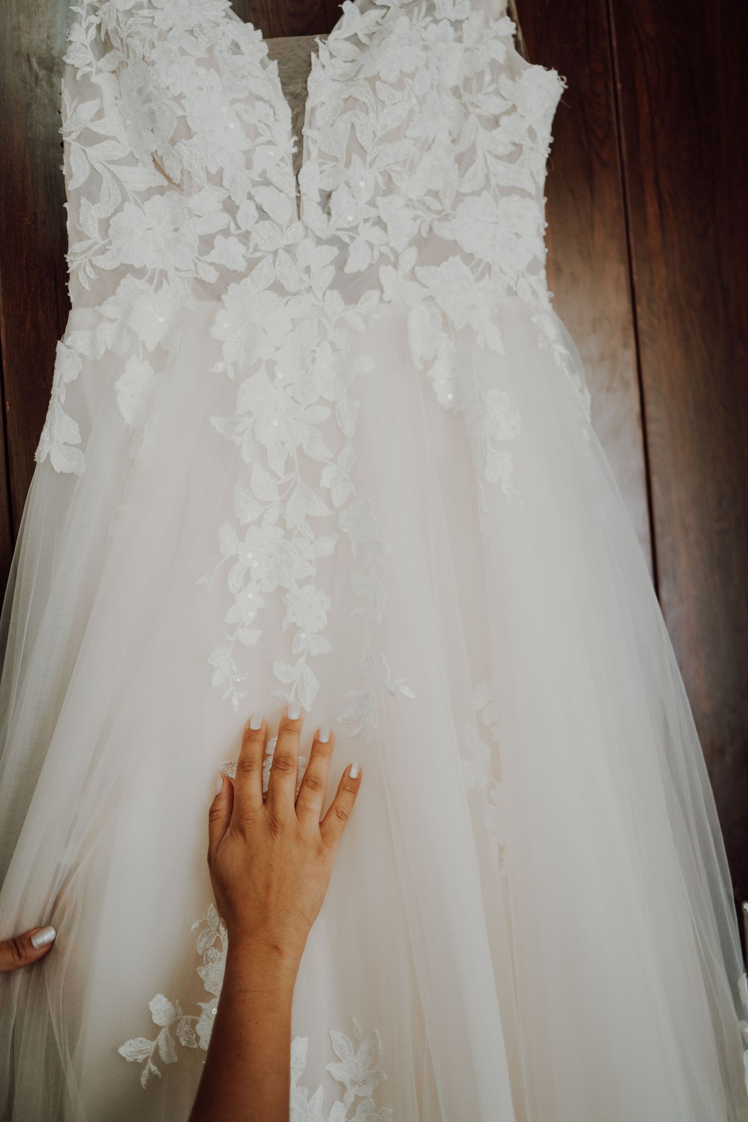 A hand reaching out to touch the delicate lace details of a white wedding gown.
