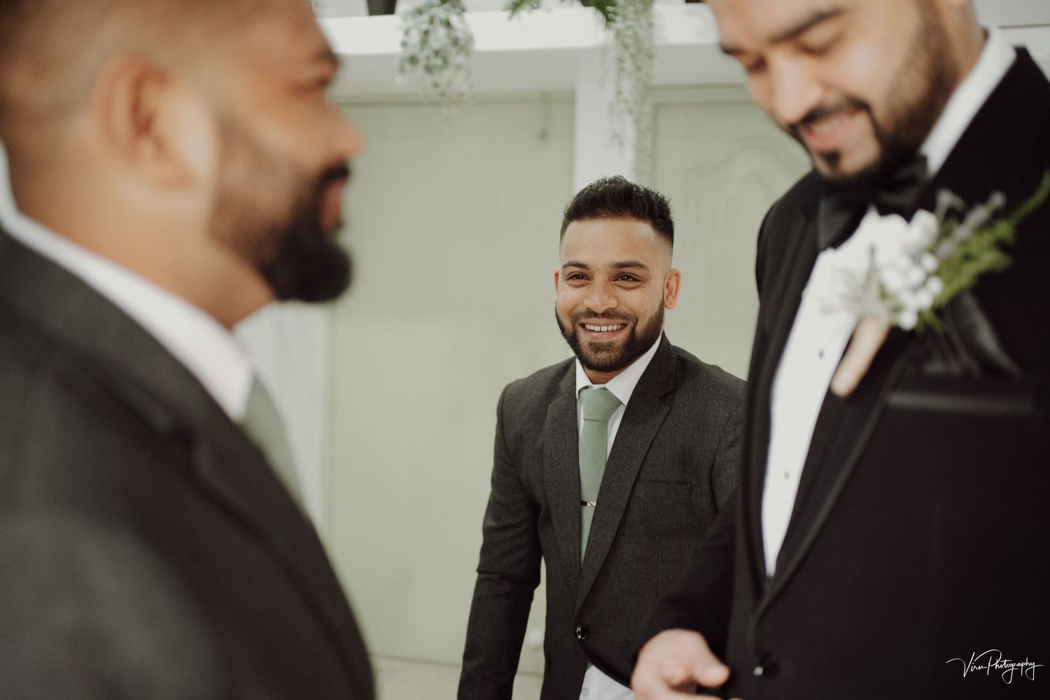 Men in suits and ties share a joyful moment at a formal event with one wearing a white boutonniere.