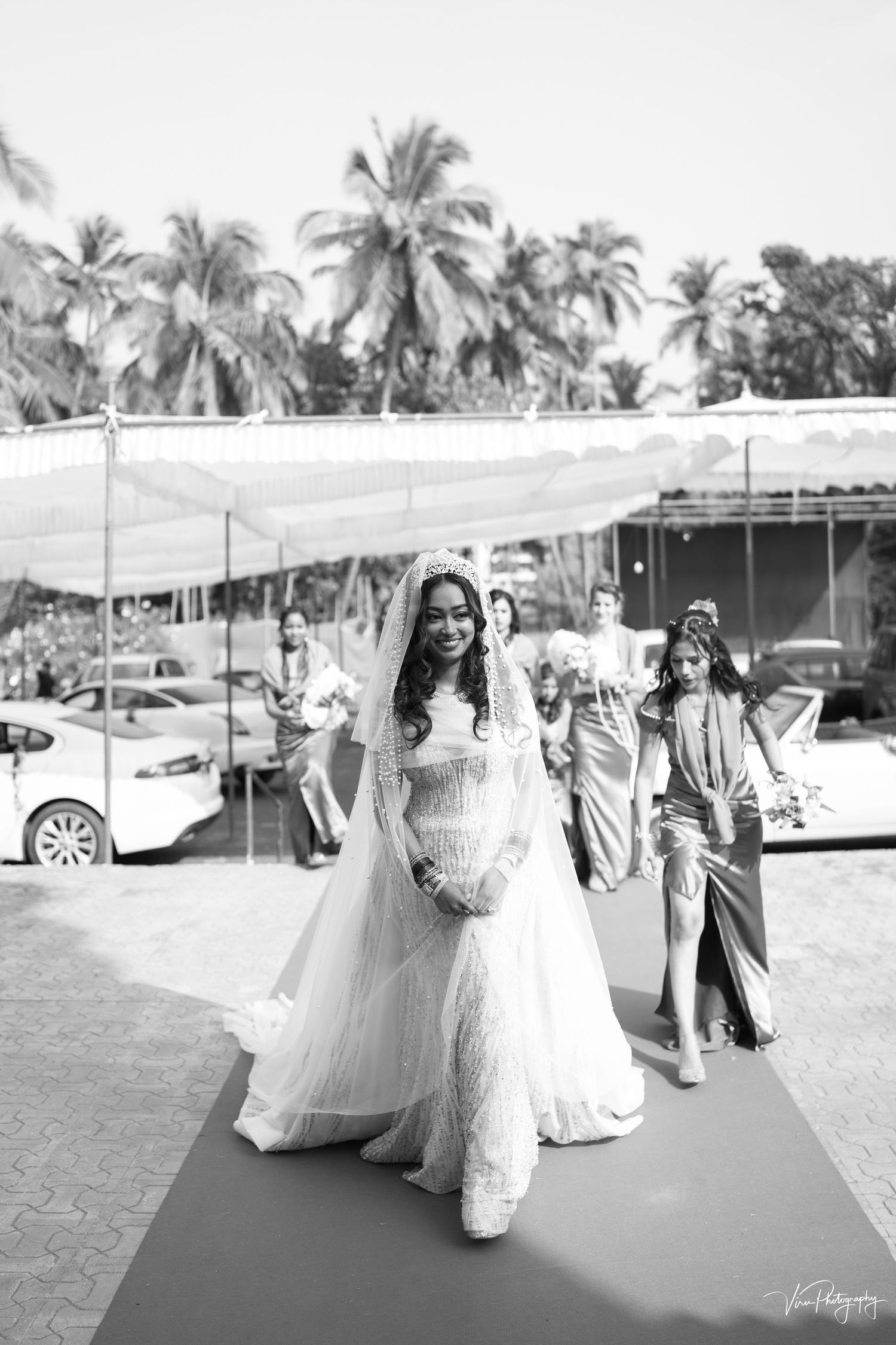A wedding scene under a tent canopy with palm trees in the background showing guests at an outdoor tropical venue.