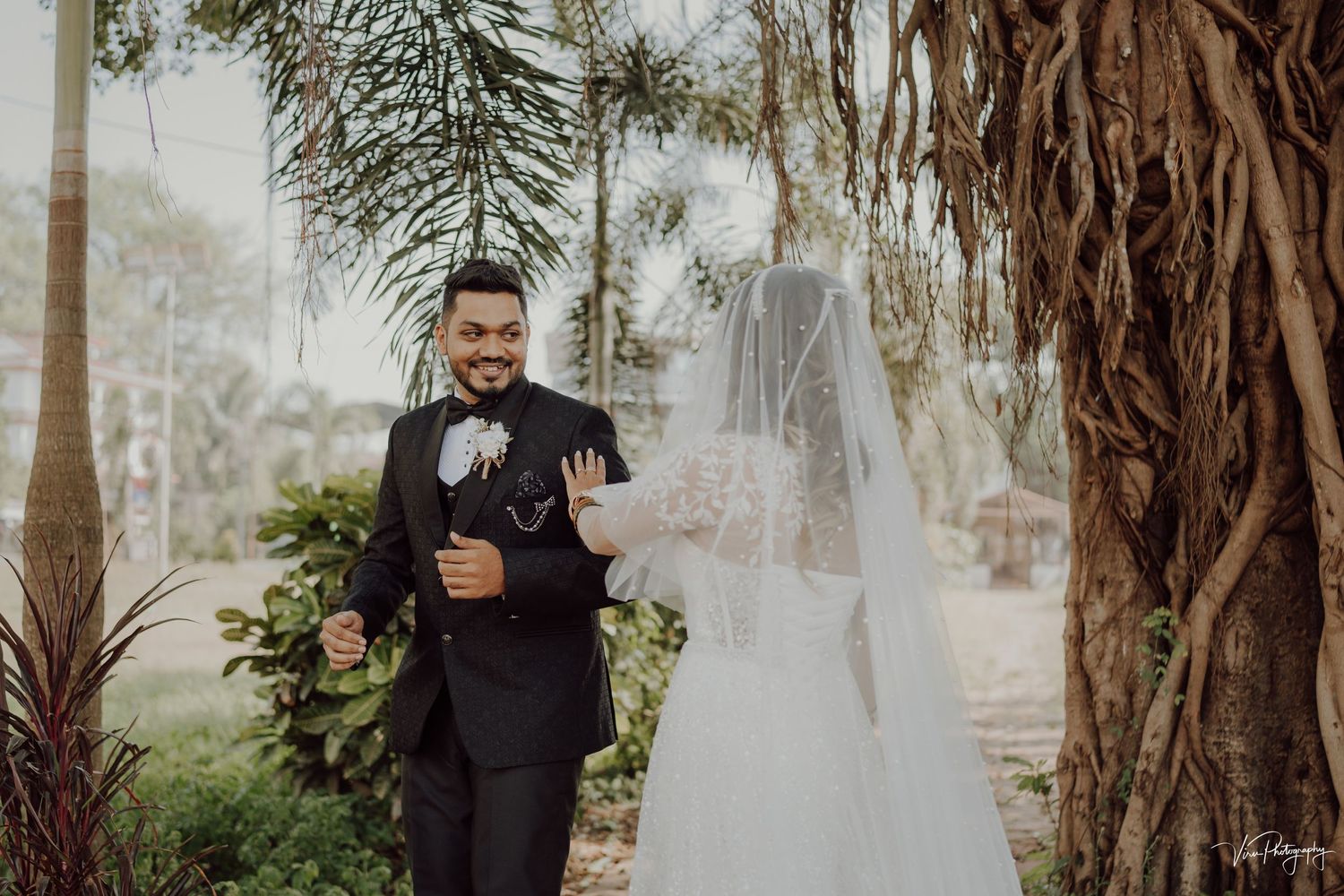 A wedding couple embraces under a beautiful banyan tree during an outdoor ceremony.