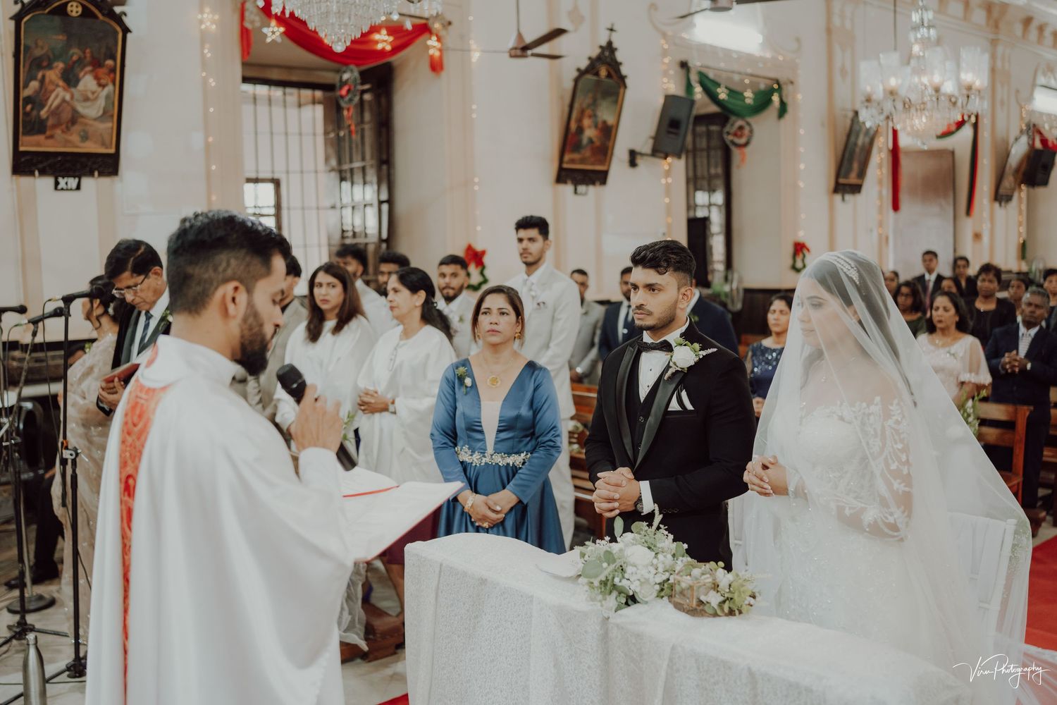 A wedding ceremony takes place inside a church with decorative lanterns hanging from above.