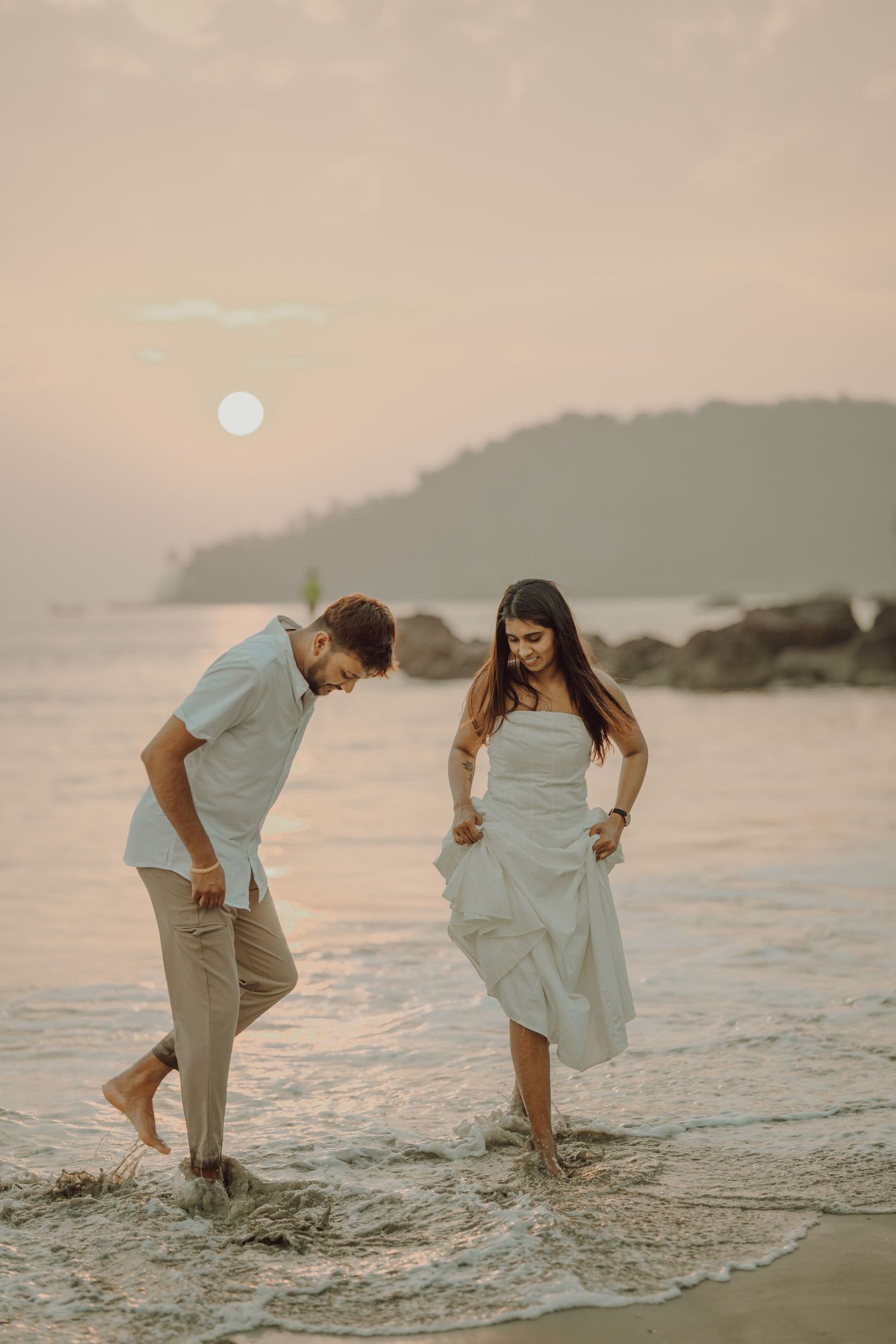 A couple playfully splashes in the ocean waves at sunset on a peaceful beach.