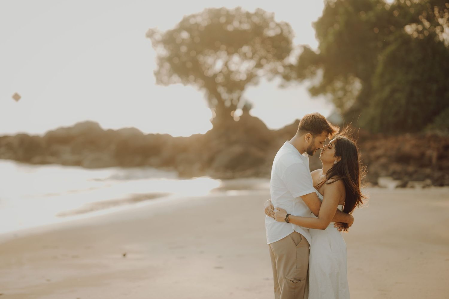 A couple embraces on a beach at sunset with warm golden light creating a romantic silhouette.