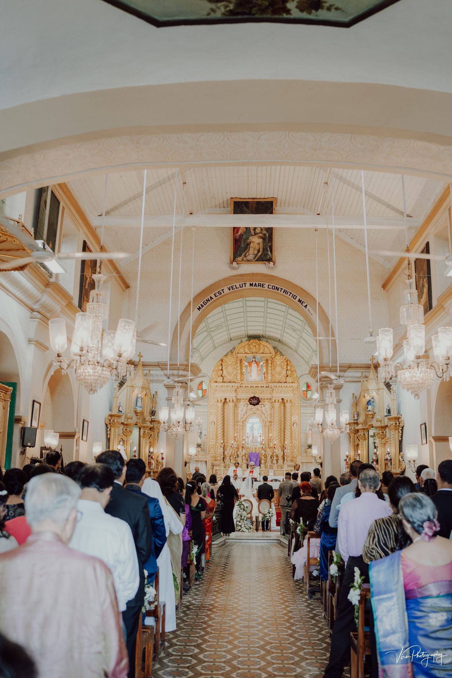 Interior view of a Catholic church during a ceremony with ornate golden altar and crowded pews.