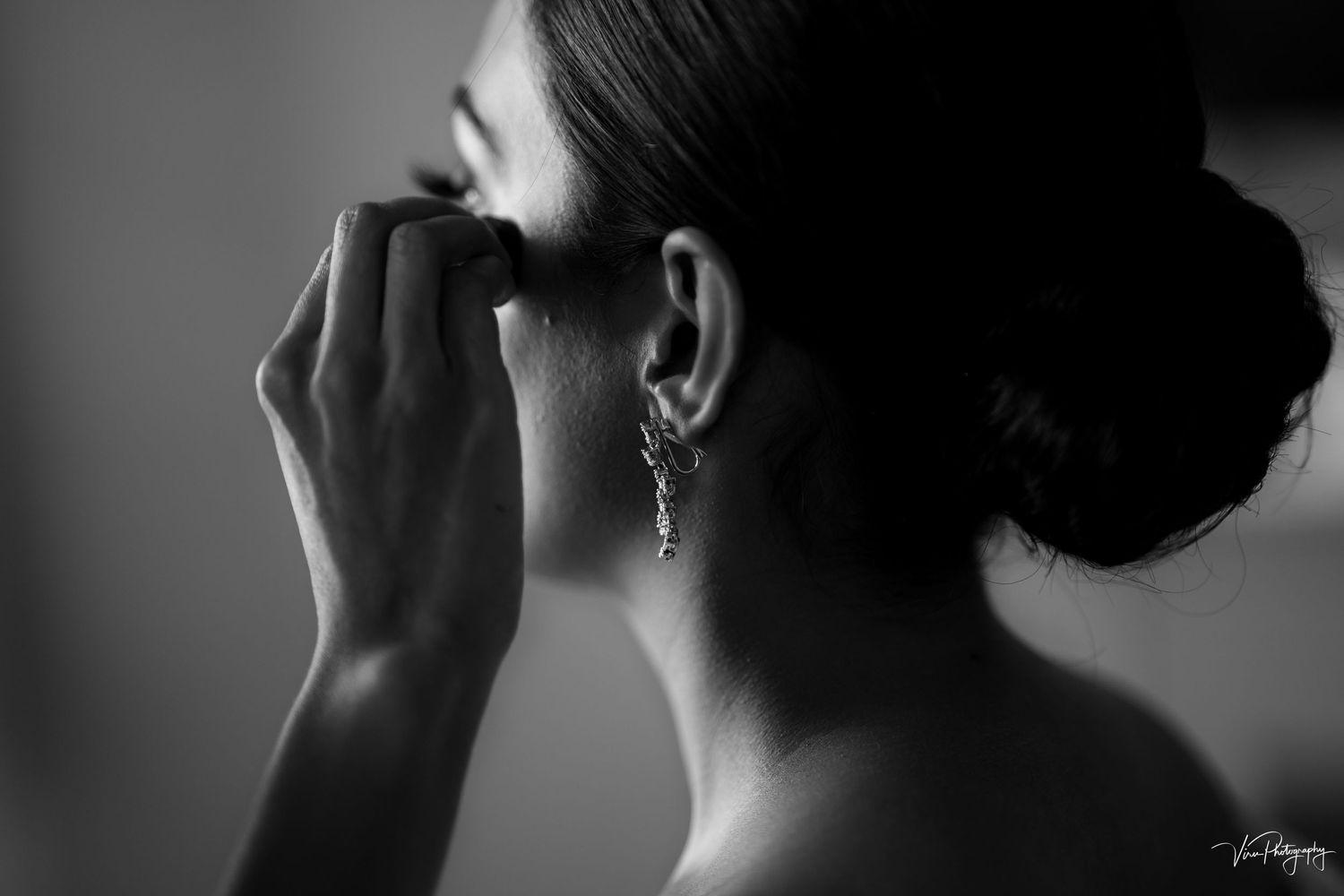 Black and white profile shot showing an elegant pearl earring and upswept hairstyle in soft focus.