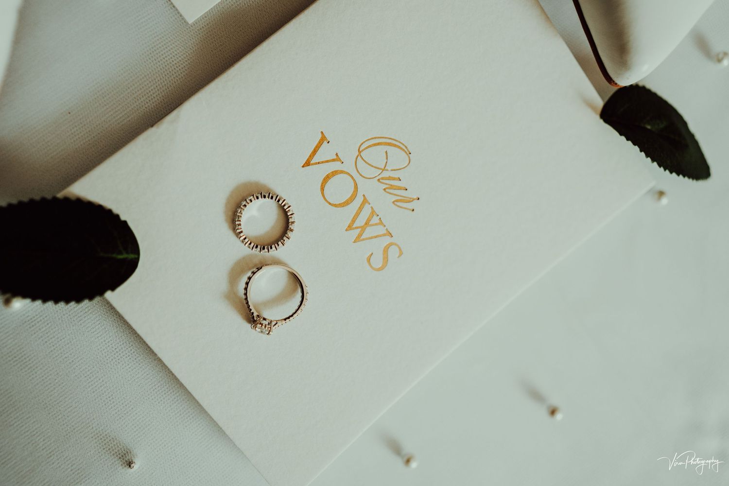 Two gold wedding rings placed on a white paper with 'LOVE' text and black feathers as decoration.