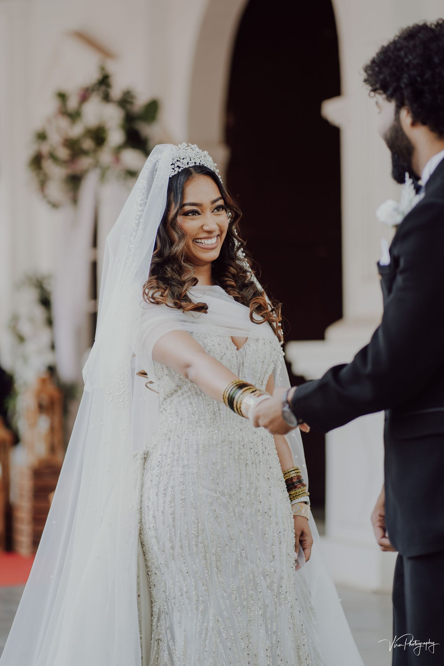 Beautiful bride in a lace wedding dress with long veil smiles during wedding ceremony exchange.
