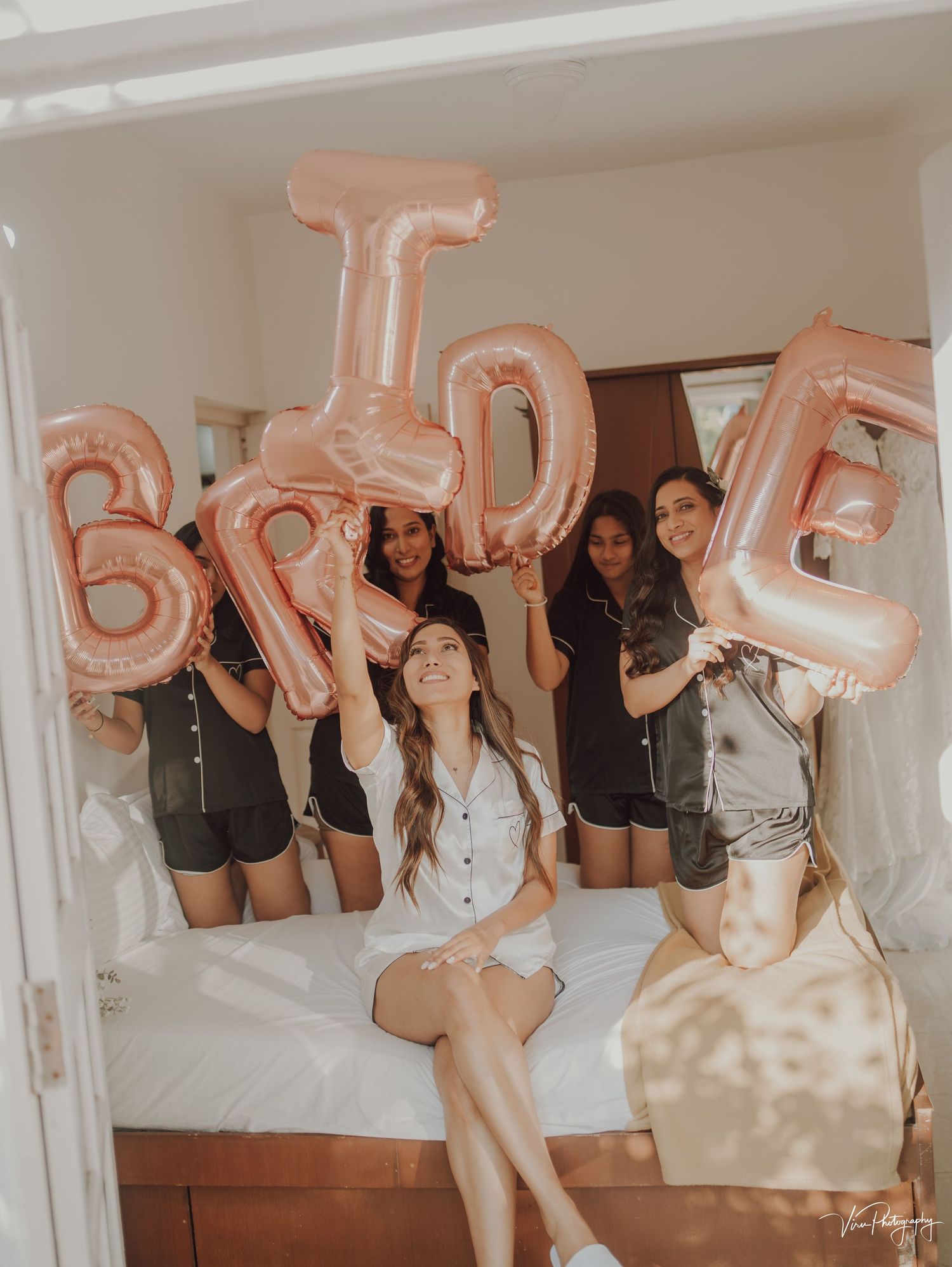 Group celebrating with rose gold BRIDE balloons in a bright indoor setting.