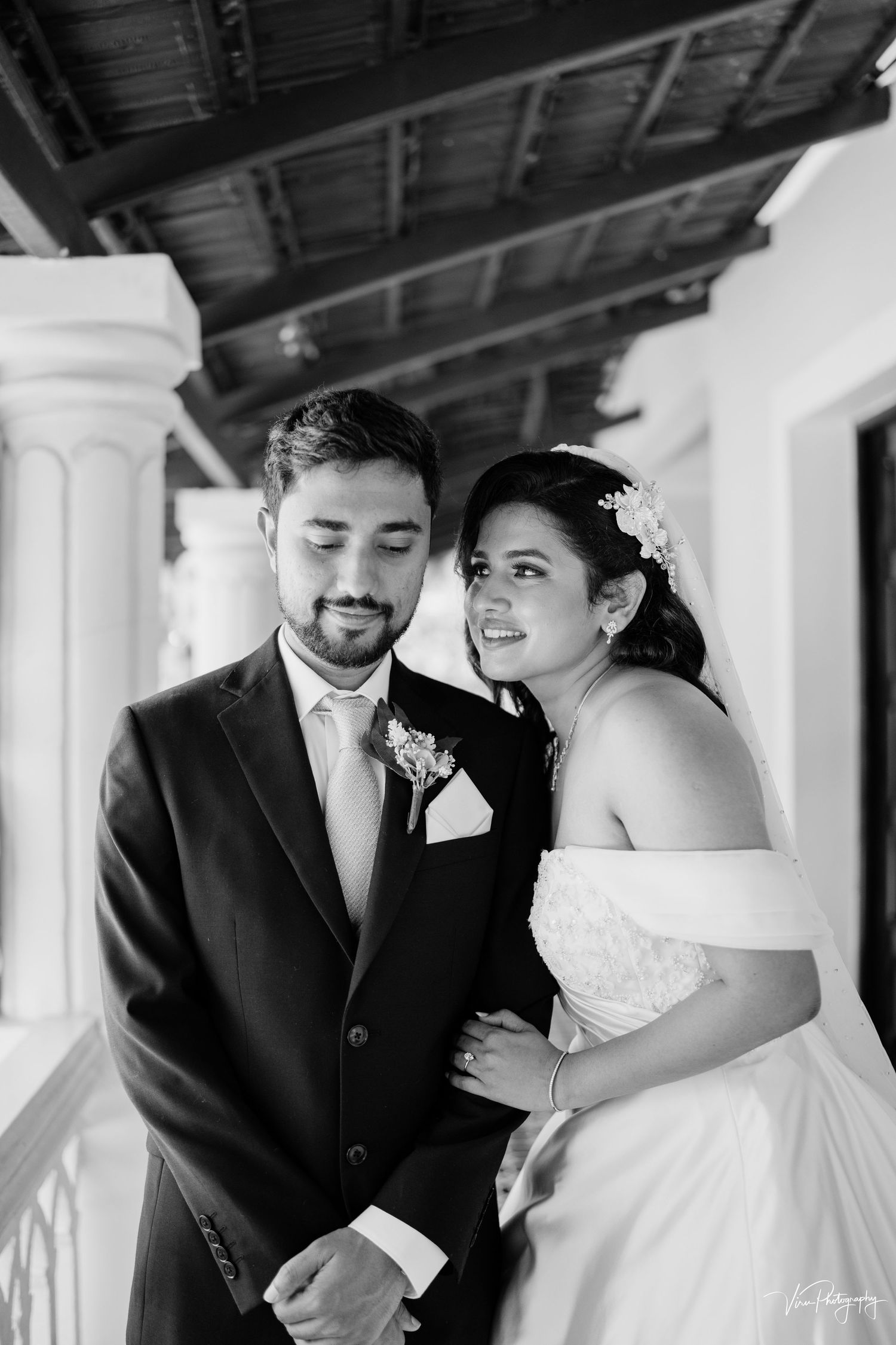 A romantic black and white wedding photo shows a couple posing together under a covered porch with classic columns.