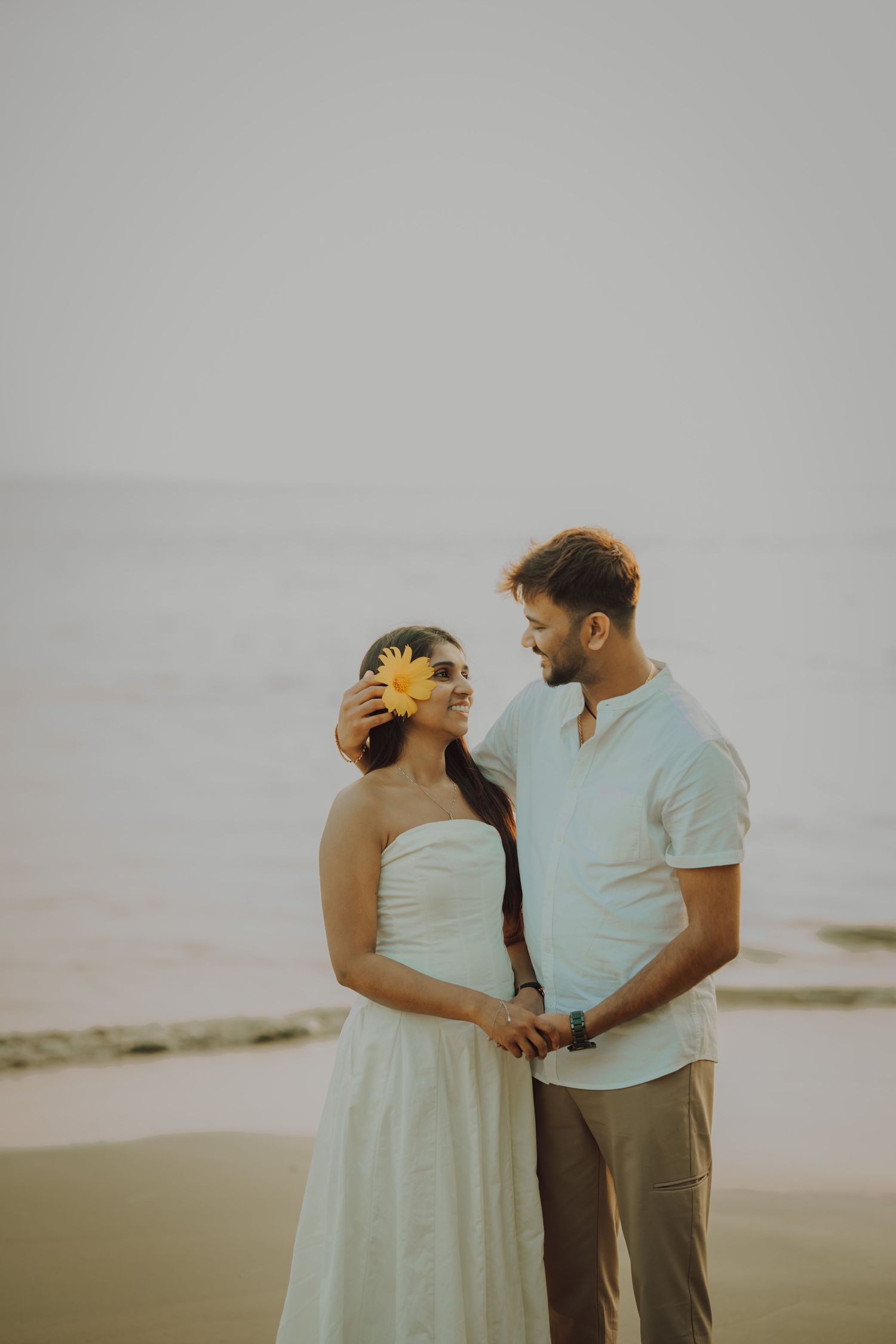 Romantic couple shares intimate moments during sunset photo session at a beach in matching light colored outfits.
