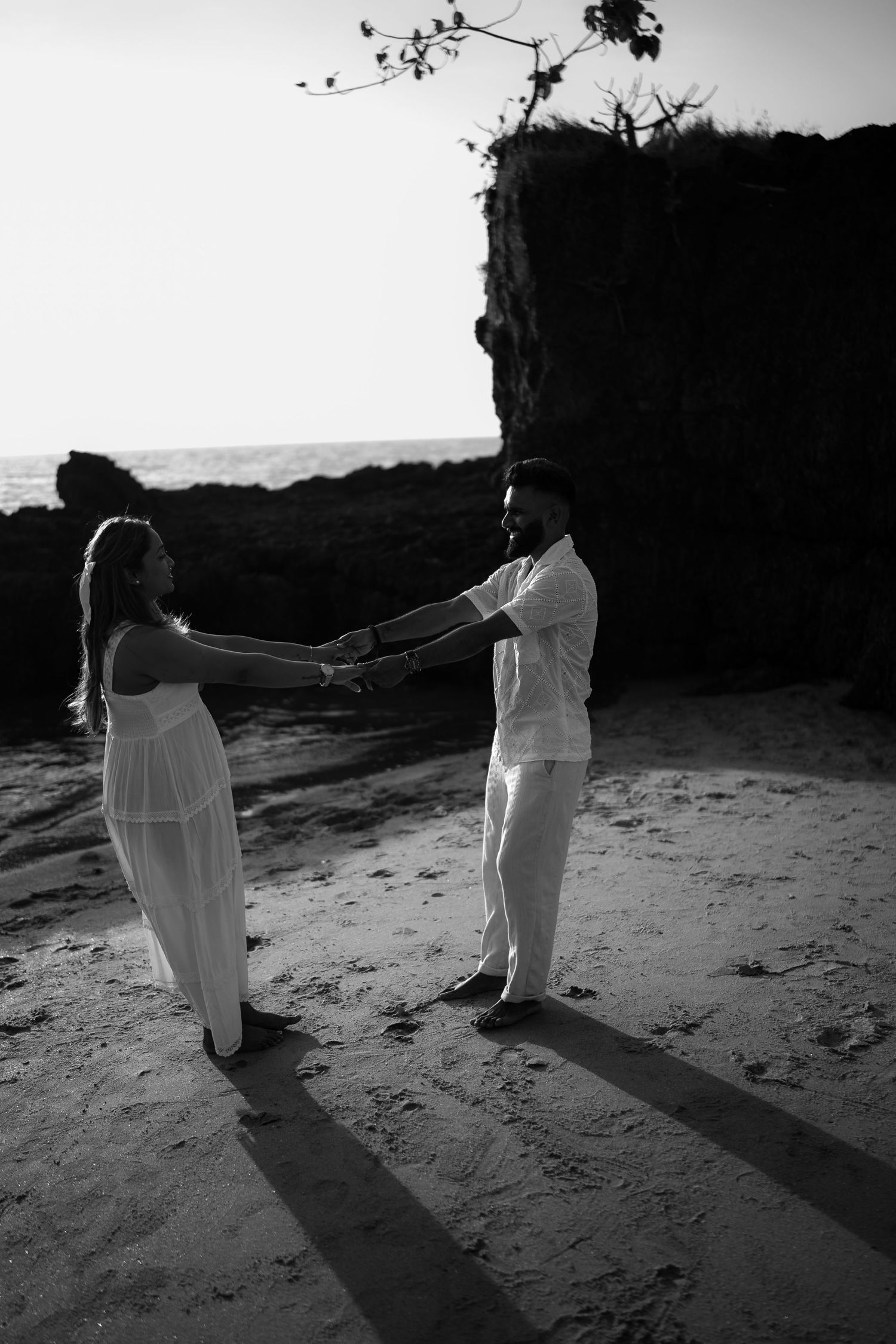 A sequence of black and white photos shows two figures in white clothing dancing together on a beach at sunset.
