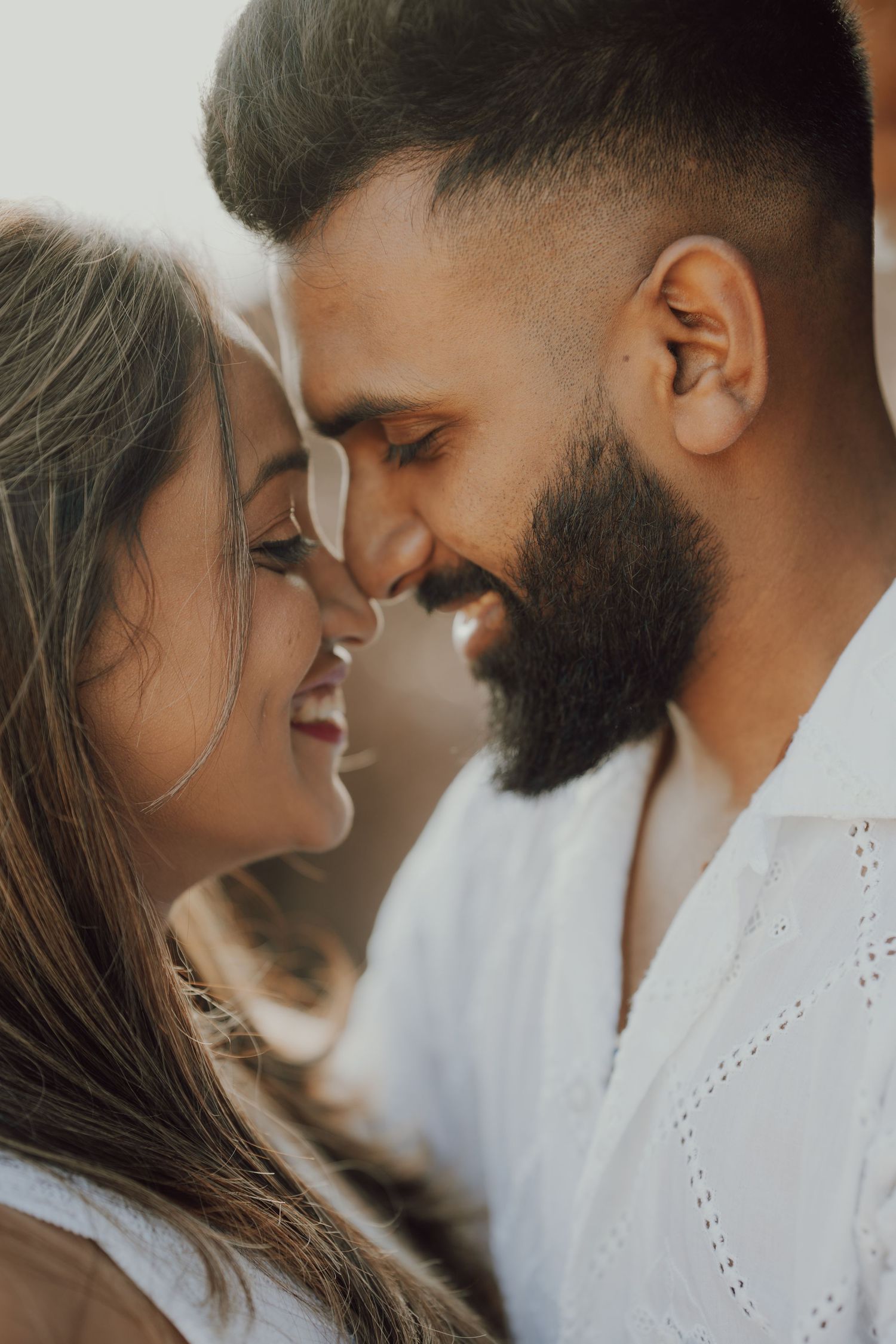 A romantic couple shares an intimate moment with their faces close together against a light background.