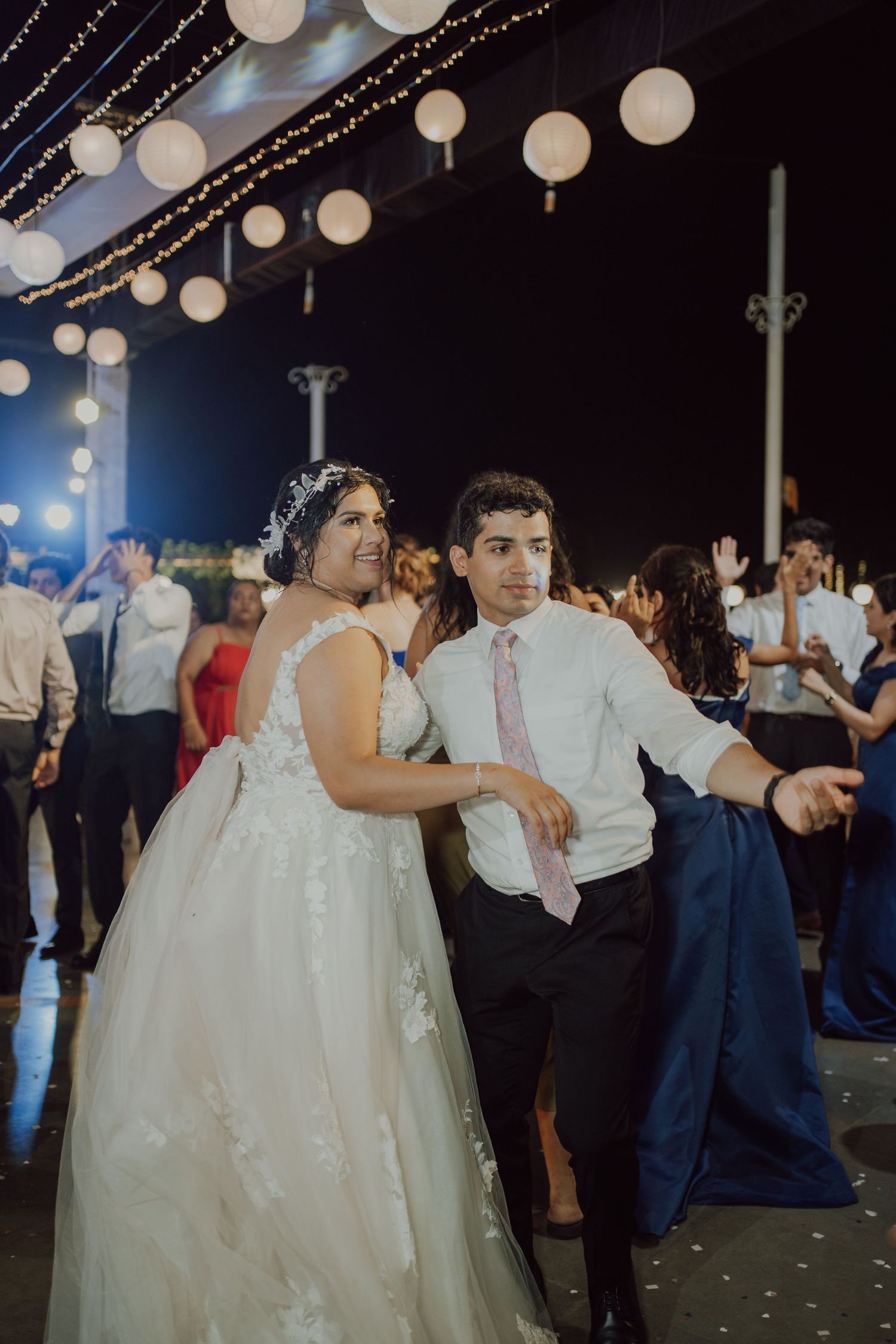 Couple dances beneath illuminated paper lanterns at nighttime outdoor wedding reception.