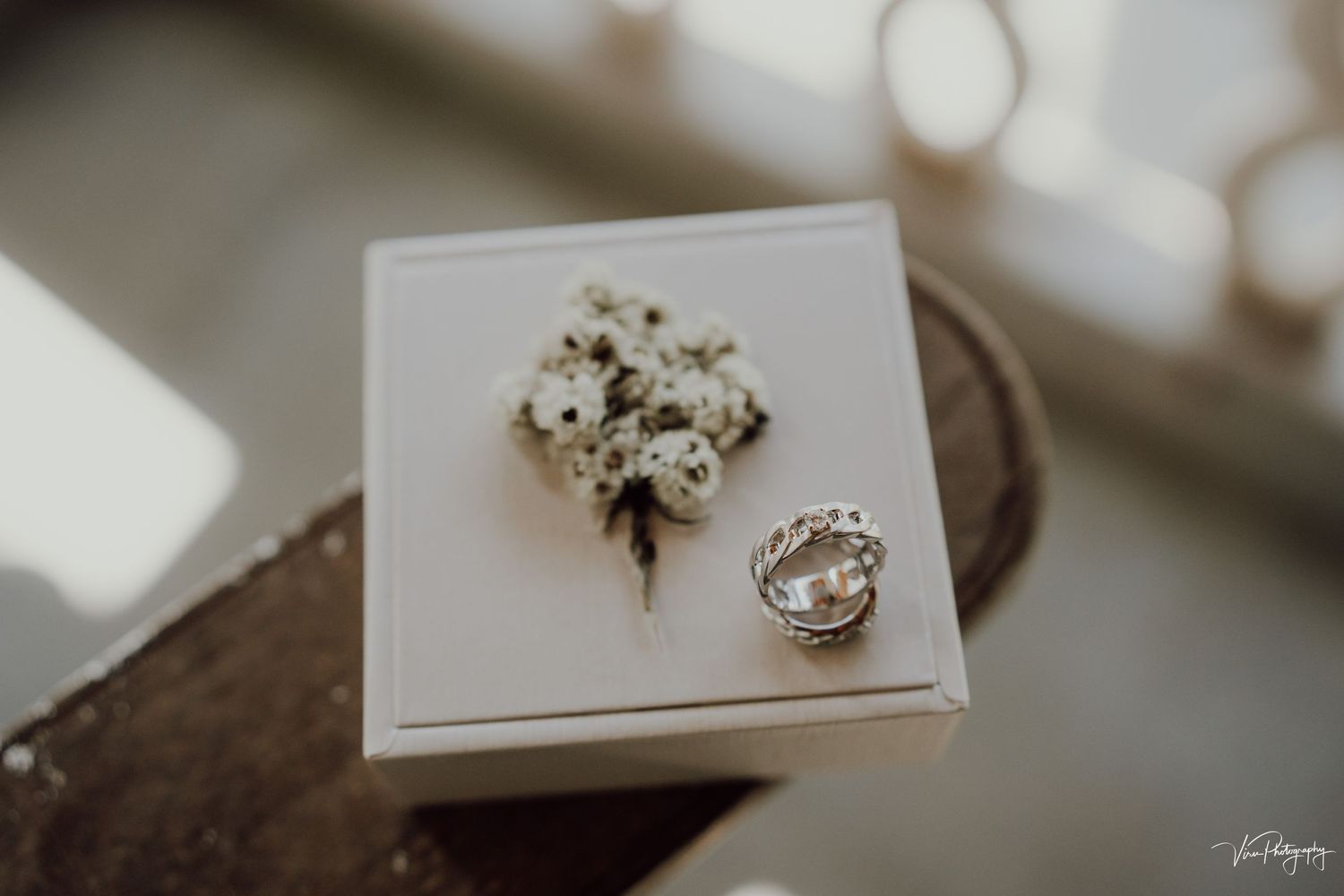 Wedding details featuring a delicate white and green boutonniere alongside a sparkling diamond ring on a white surface.