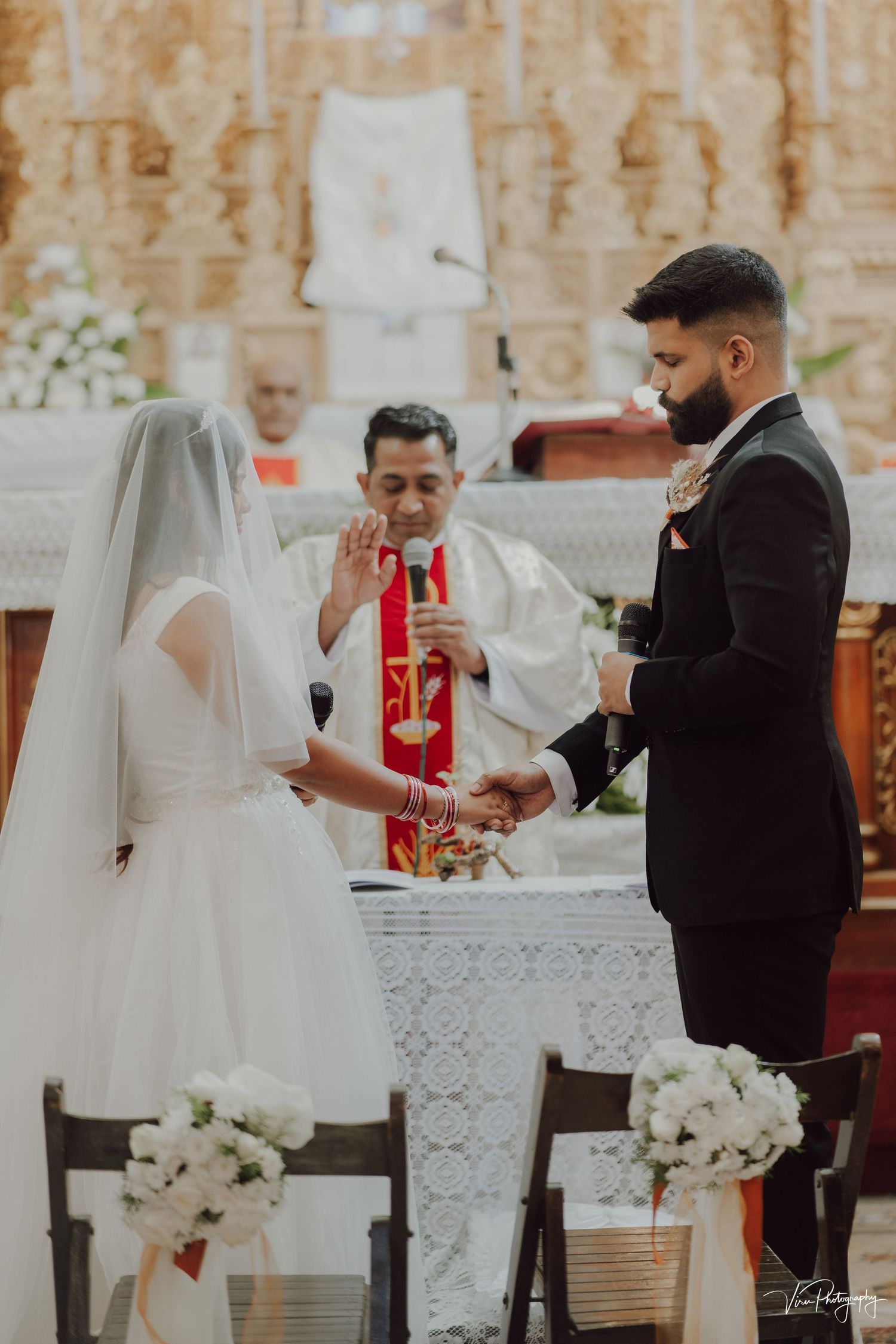Bride and groom stand at altar during traditional Catholic wedding ceremony with priest officiating in ornate church.