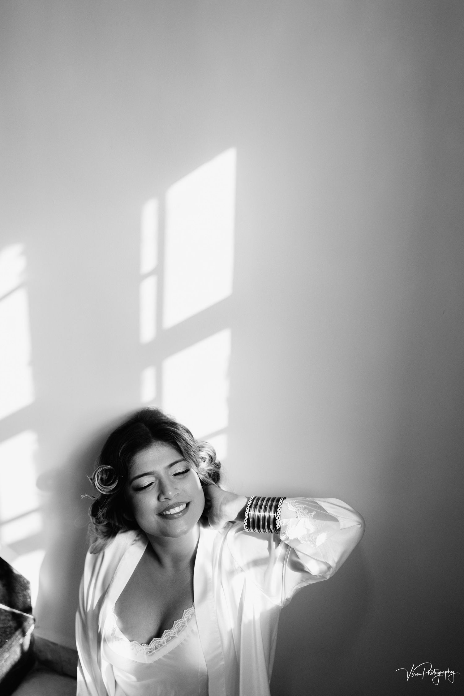 A monochromatic boudoir photo with sunlight streaming through windows creating dramatic shadows and highlights.