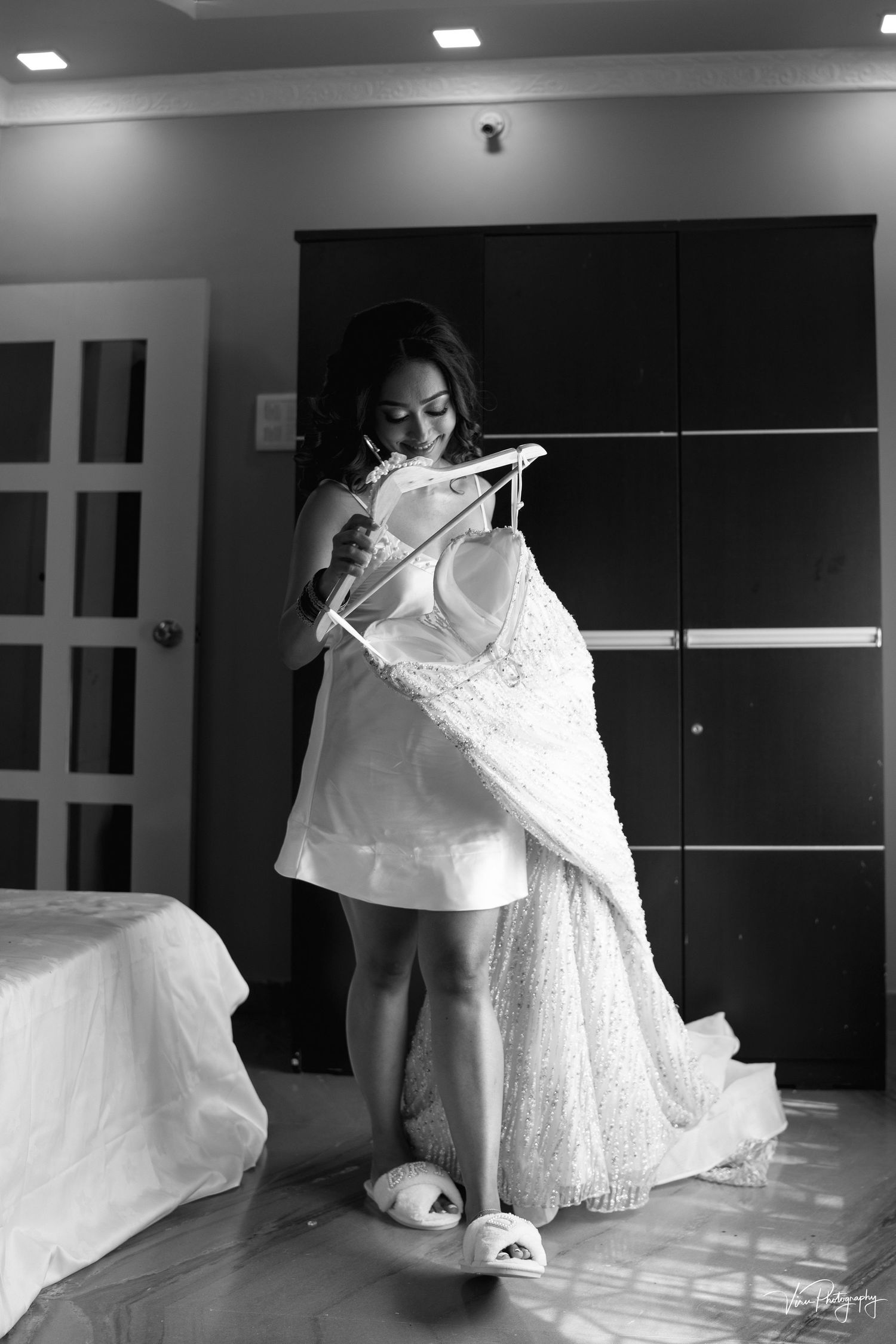 Black and white photo showing preparation with a wedding dress and cozy slippers in a modern hotel room interior.