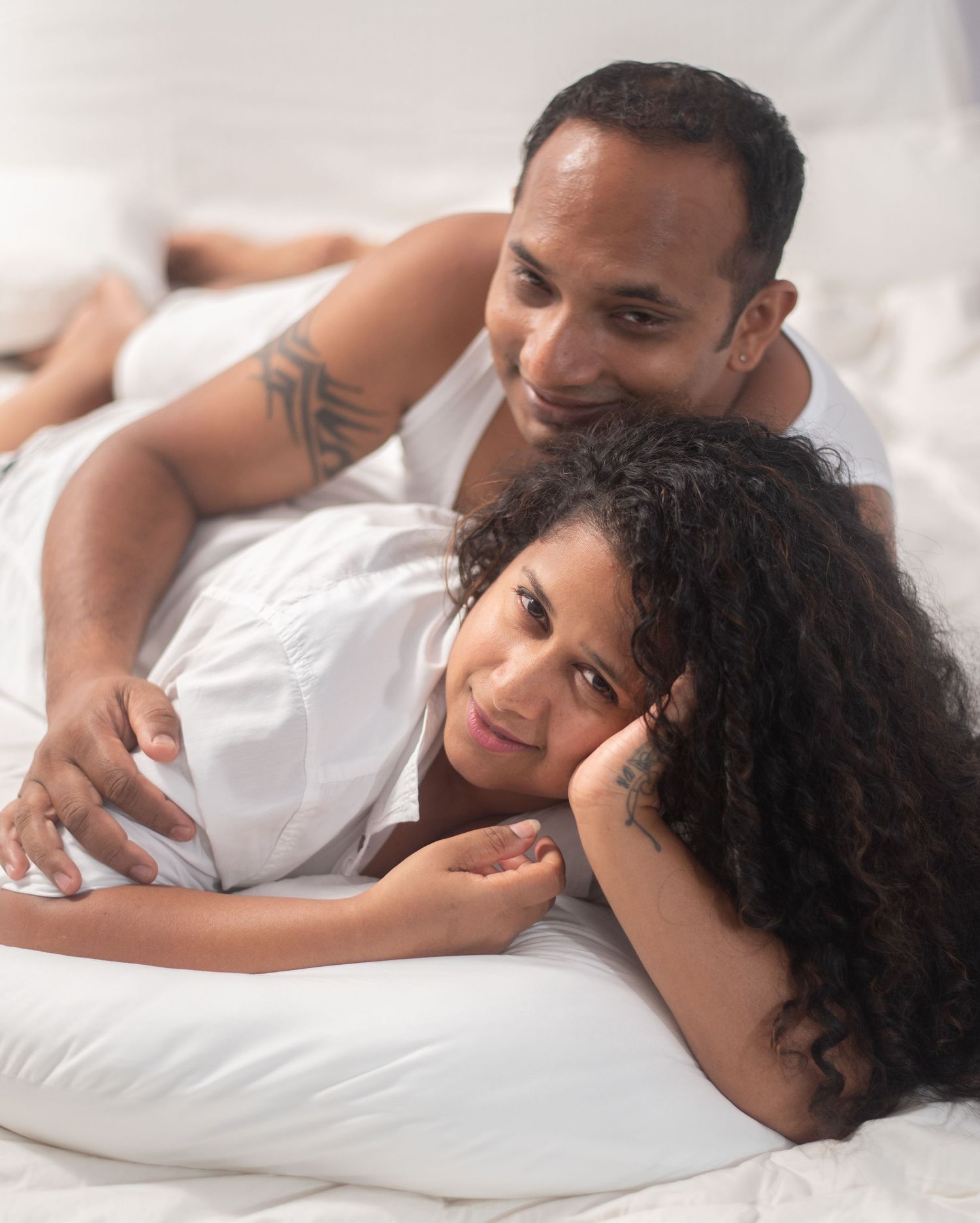 Intimate couple lying together in bed with white sheets showing affection and closeness.